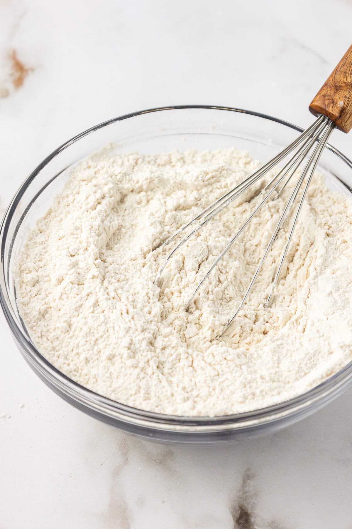 dry ingredients for vanilla cake being whisked in a clear glass bowl