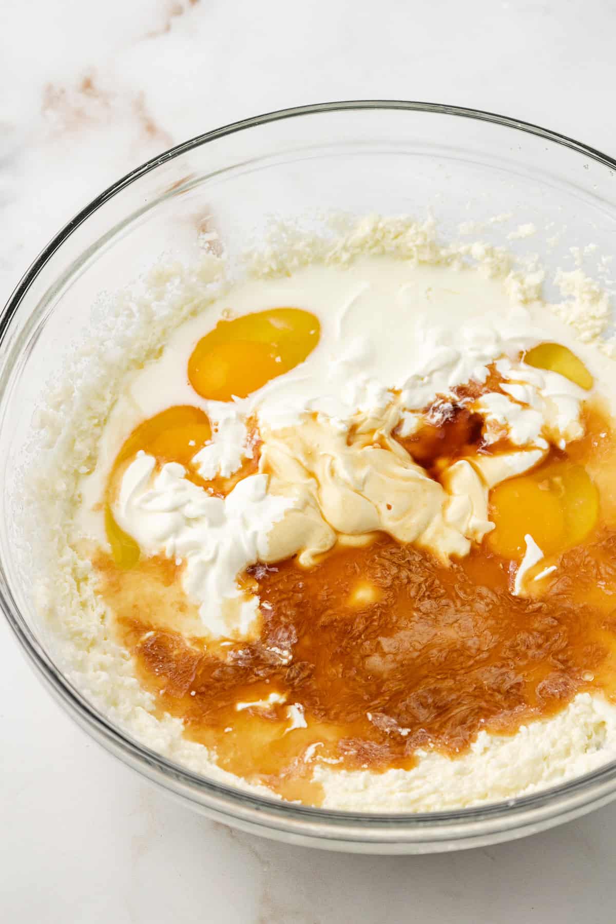 eggs, sour cream, milk, and vanilla extract on top of other vanilla cake ingredients in a clear glass bowl