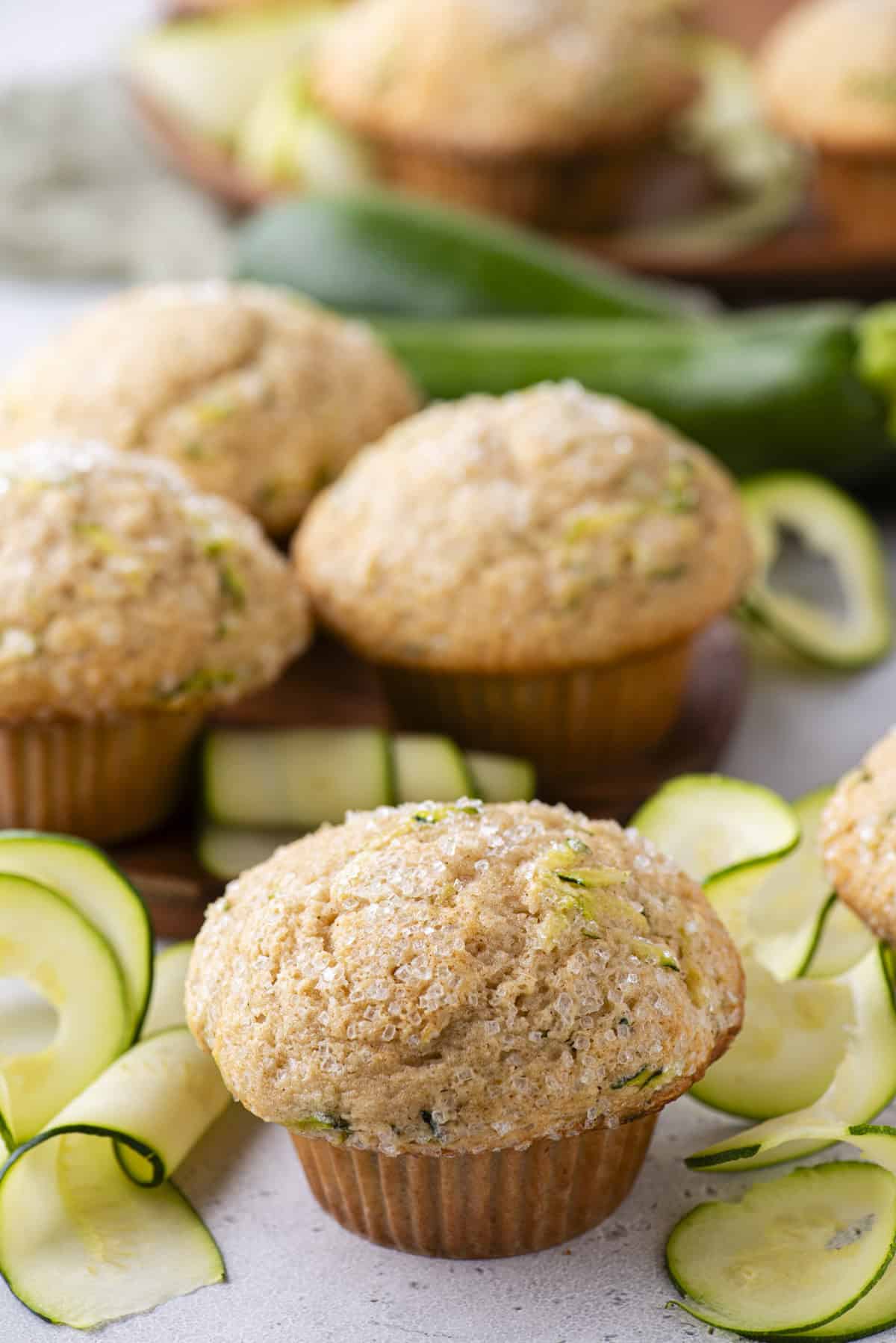 a zucchini muffin with zucchini slices around it and more muffins and whole zucchinis in the background