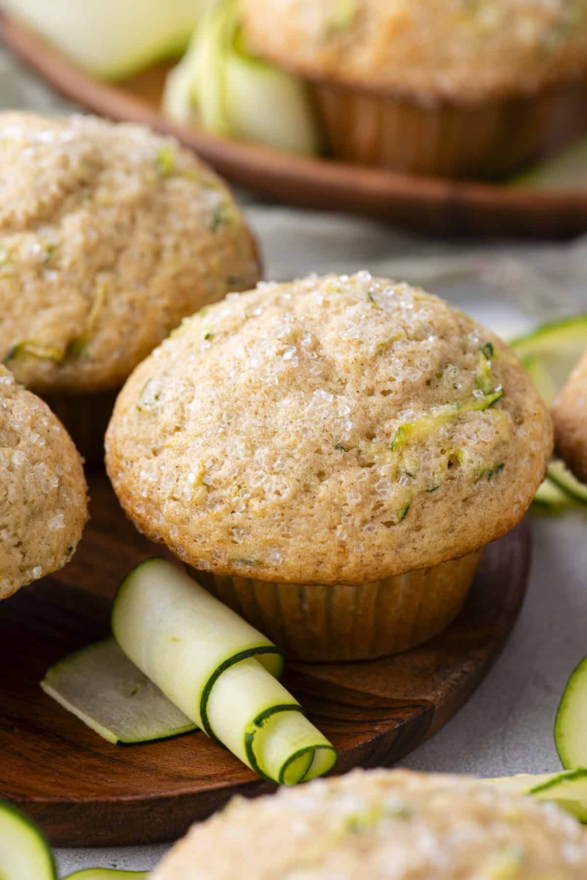 zucchini muffins on a wood plate with more muffins and thin slices of zucchini scattered around