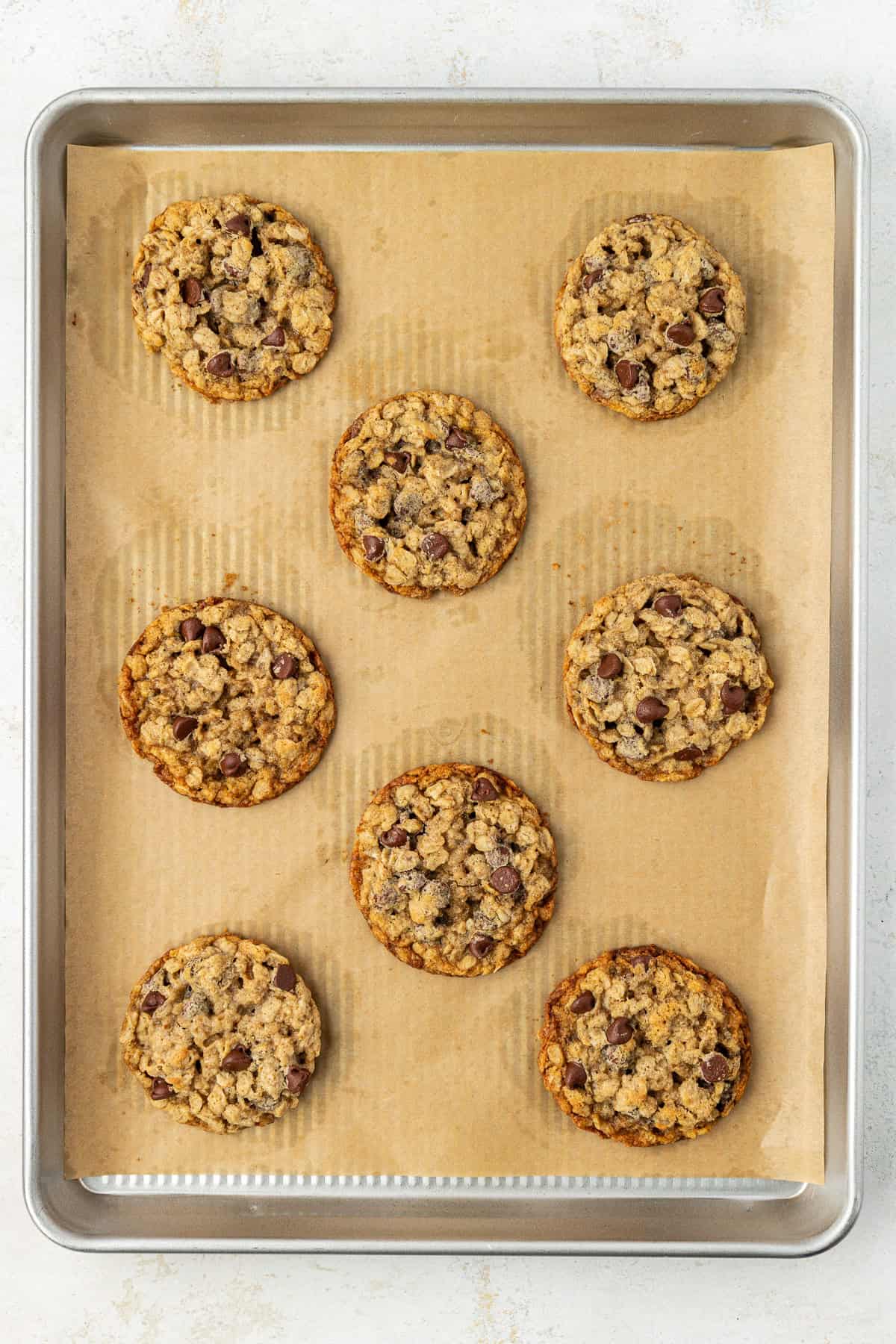 over head view of chocolate chip oatmeal cookies baked on a baking sheet lined with brown parchment paper