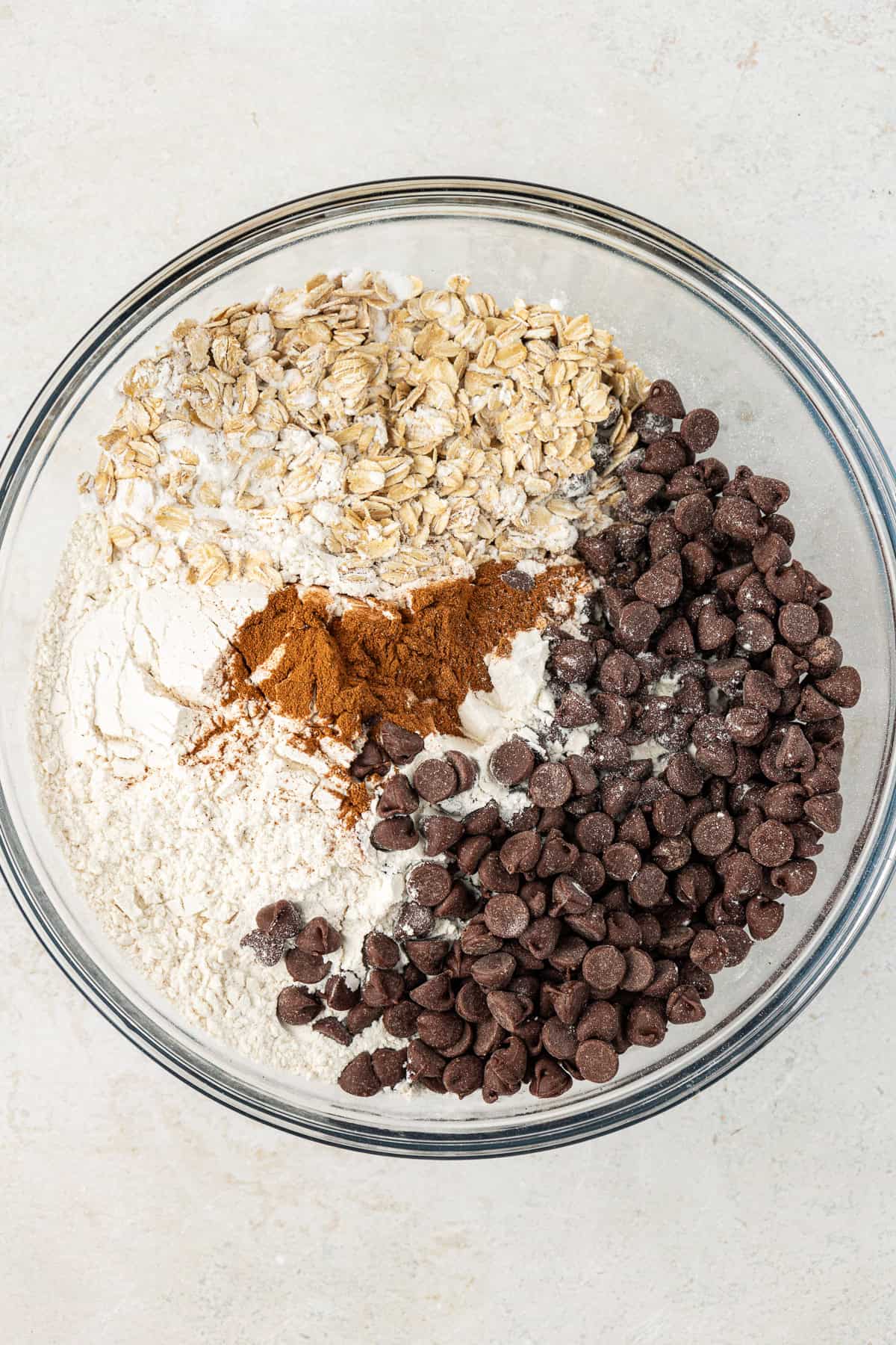 dry ingredients for oatmeal chocolate chip cookies in a clear glass bowl including flour, cinnamon, oats and chocolate chips