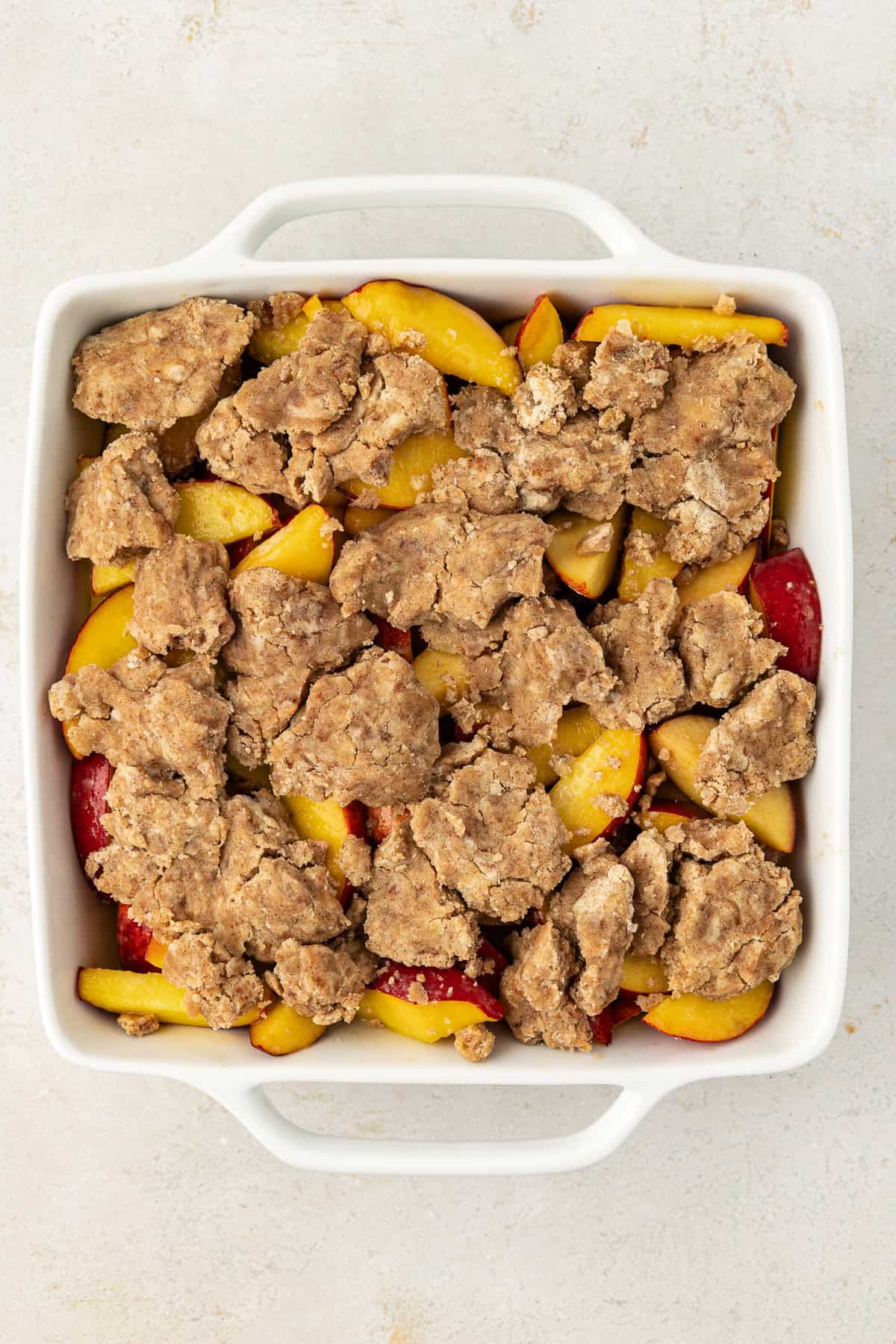 peach cobbler ready to be baked in a square white baking dish