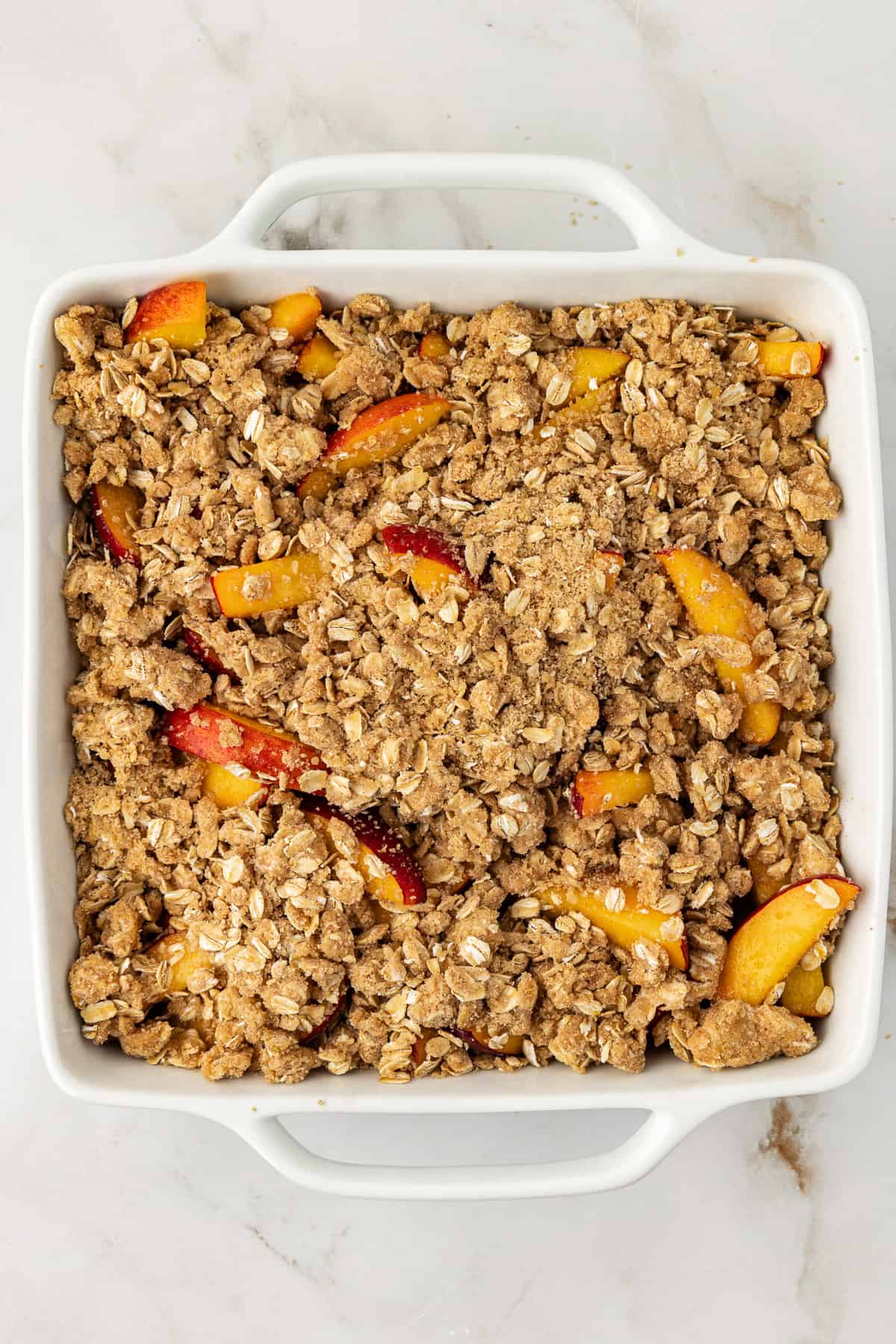 overhead view of a peach crisp in a square baking dish before it has been baked