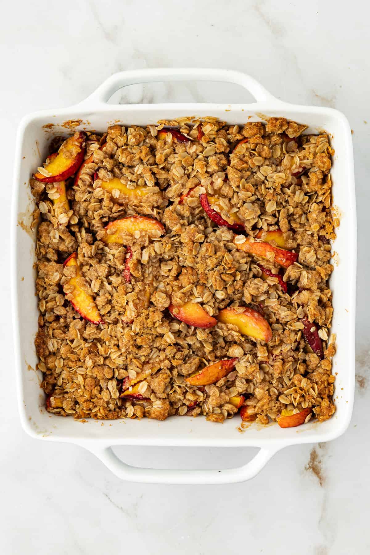 overhead view of peach crisp baked in a square white baking dish