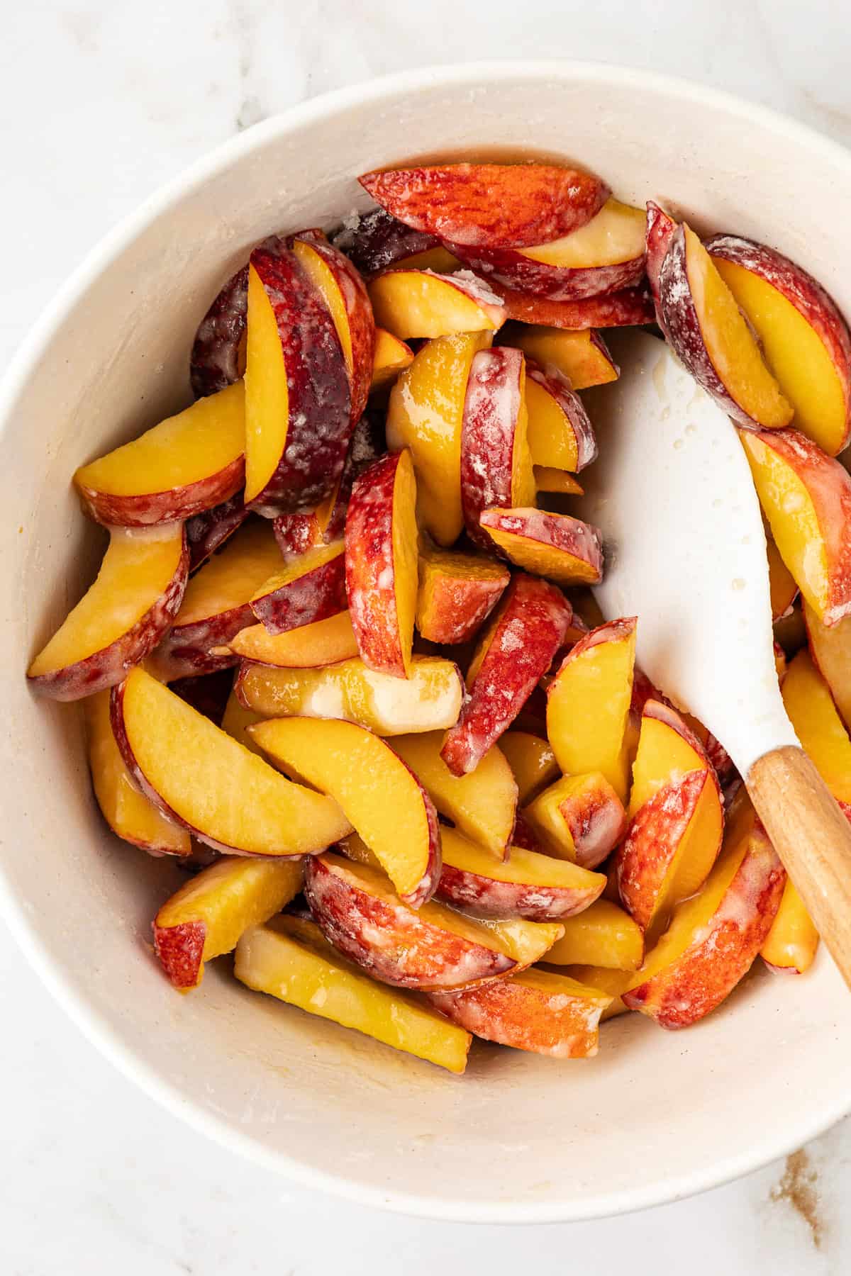 a bowl of sliced peaches being mixed for peach filling in a white bowl with a white and wooden spatula