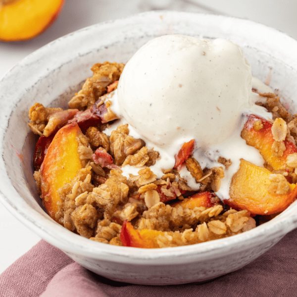 a small white bowl with a serving of peach crisp with a scoop of vanilla ice cream