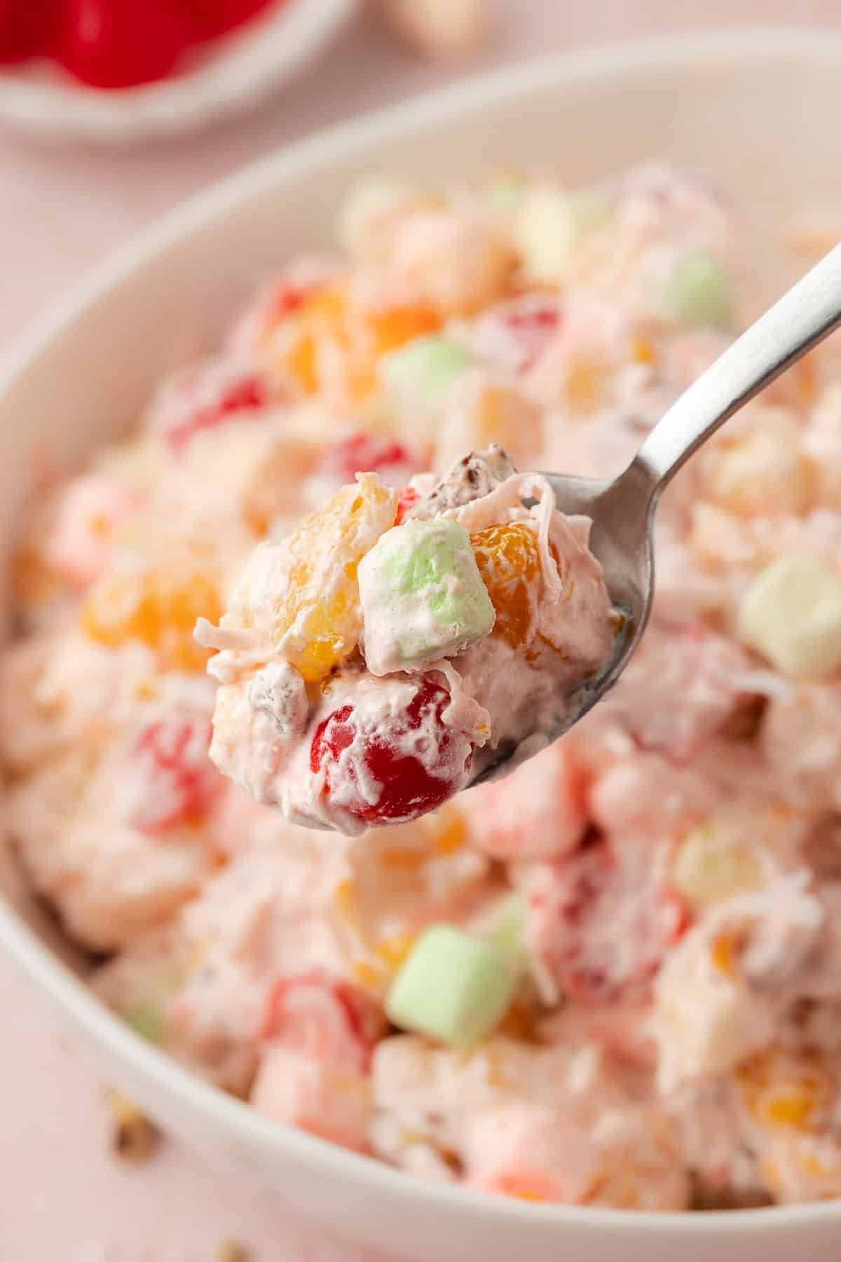 a spoon full of ambrosia salad being lifted over top of a bowl of ambrosia