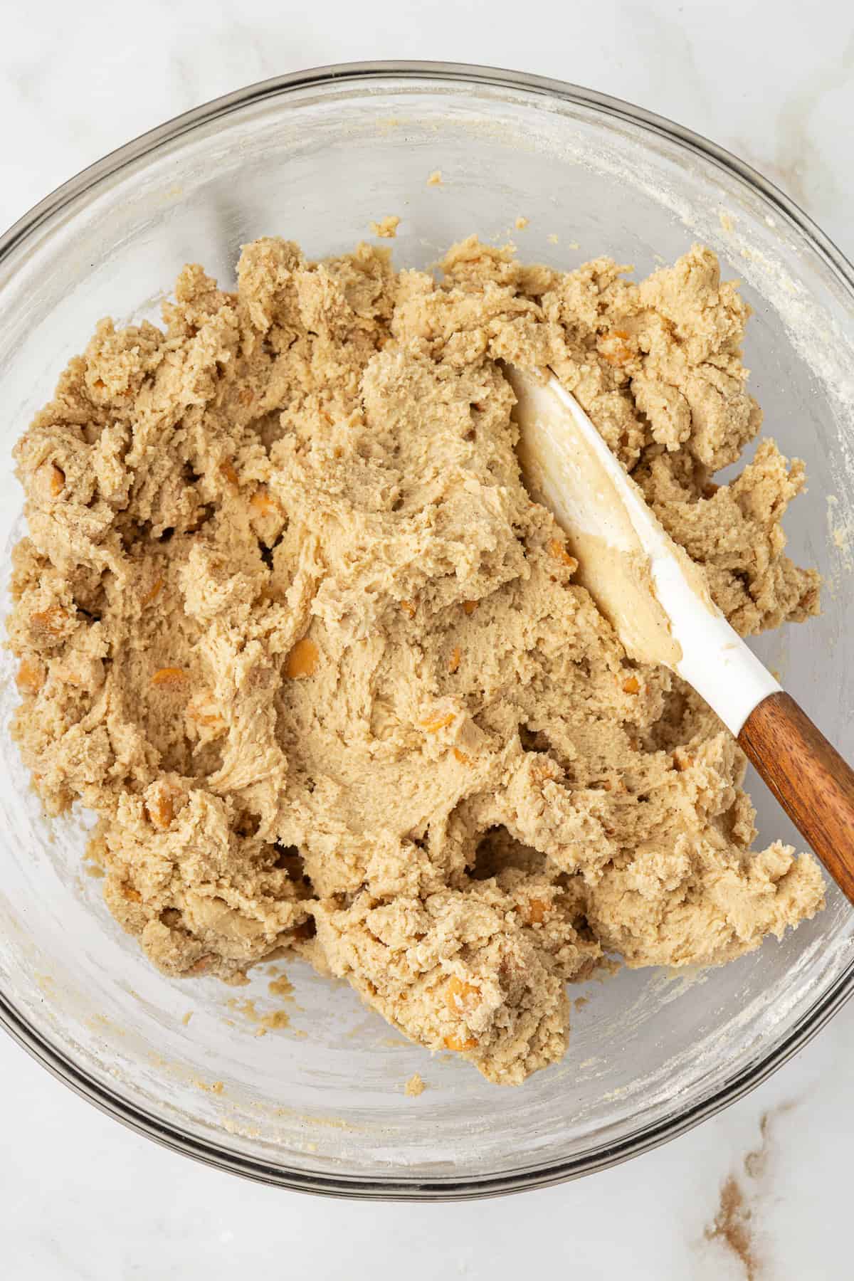 butterscotch cookie dough in a clear glass bowl with a white spatula leaning inside of it