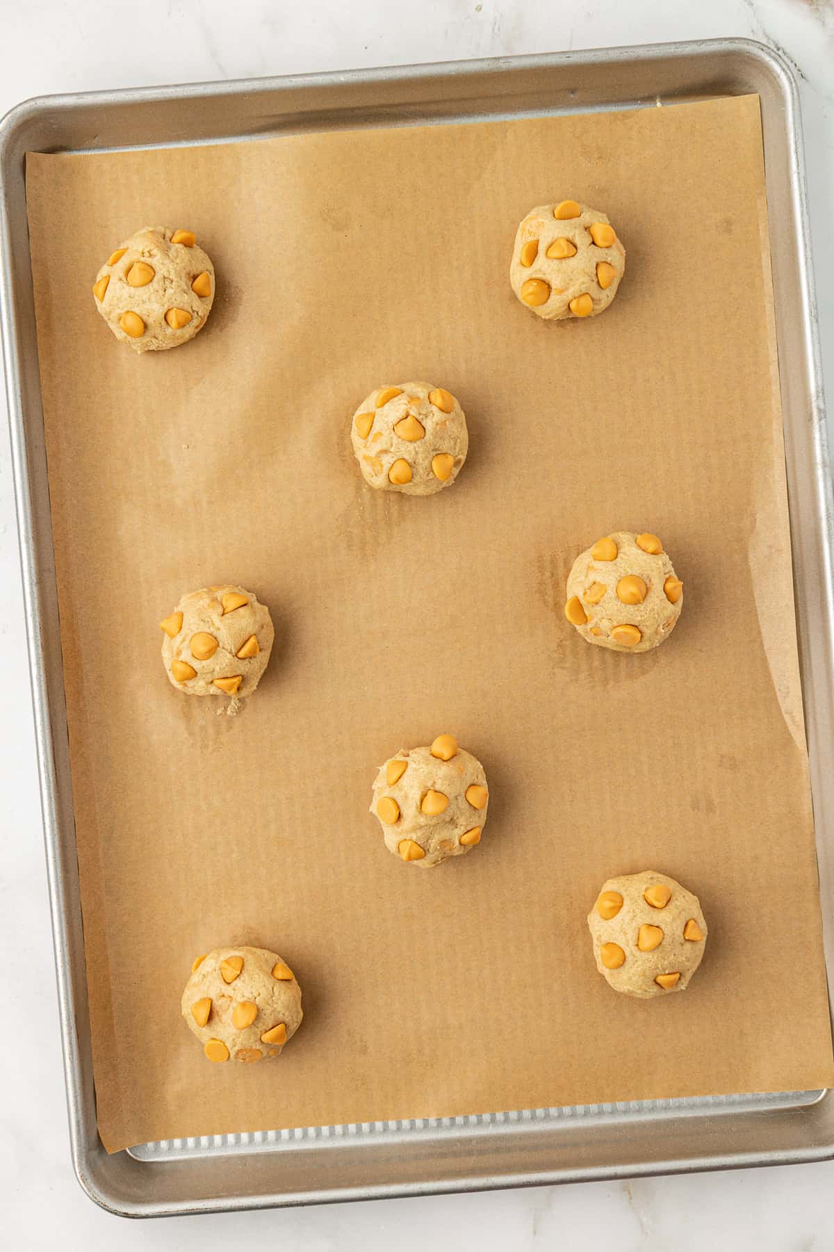 over head view of butterscotch cookie dough balls on a baking sheet lined with parchment paper