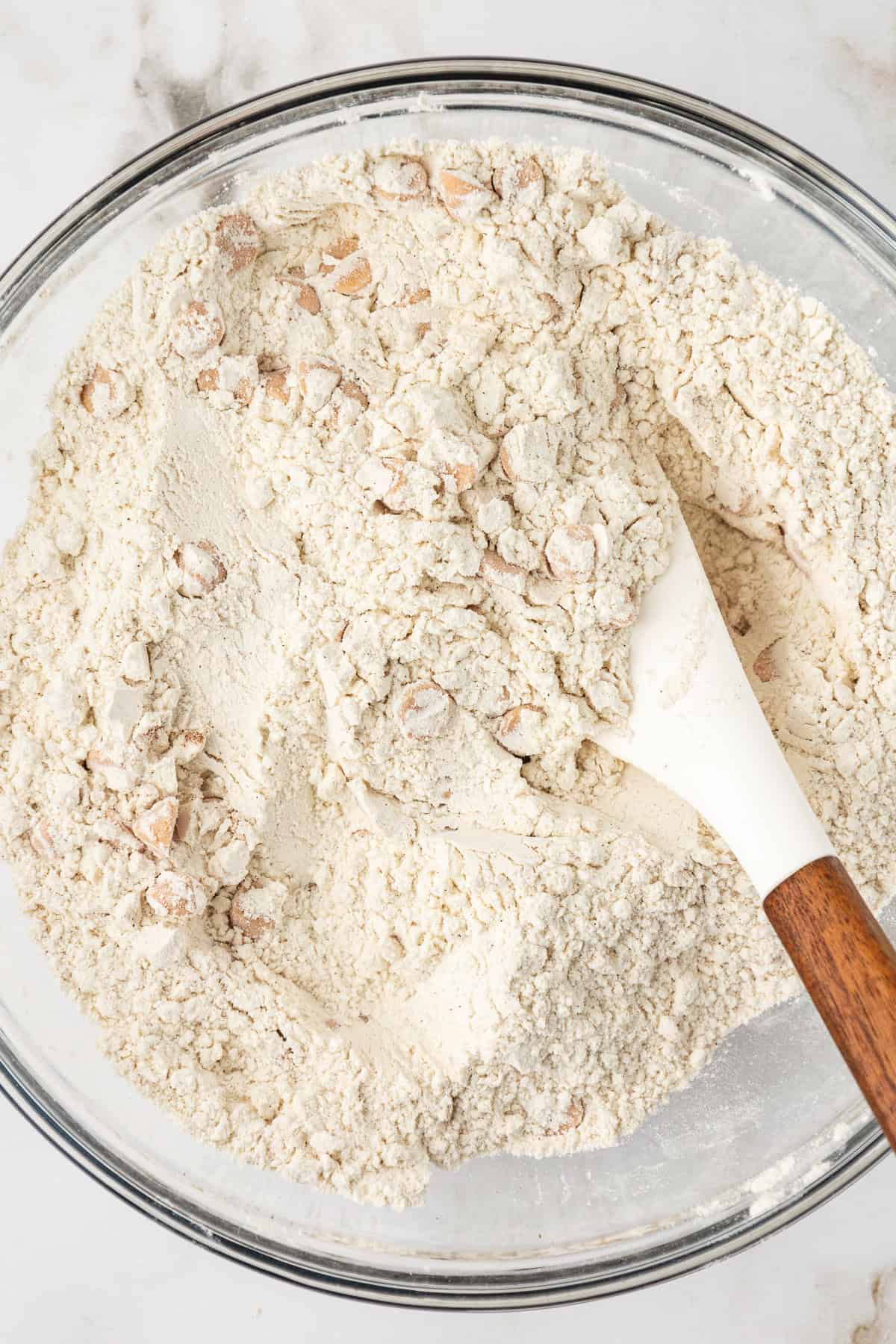 dry ingredients for butterscotch cookies being mixed in a clear glass bowl with a white spoon