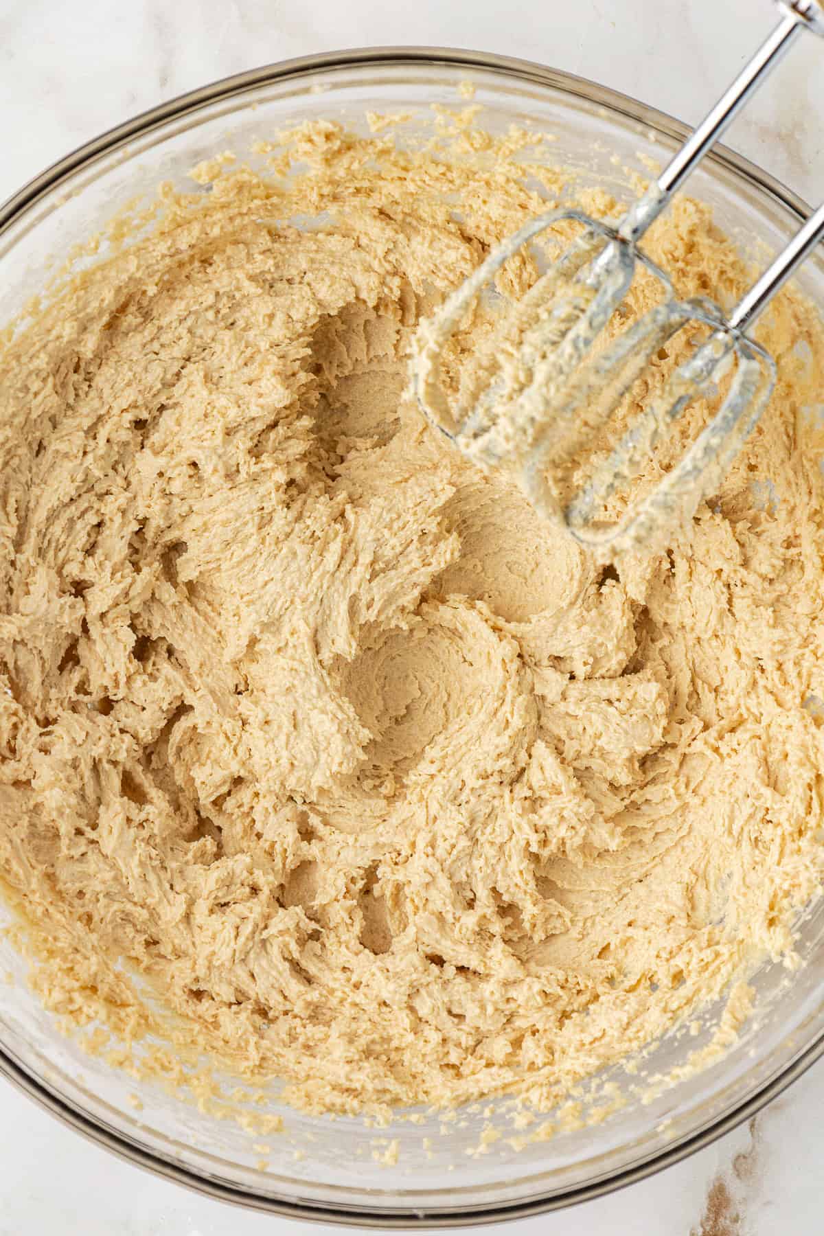 wet ingredients for butterscotch cookies combined in a clear glass bowl with an electric mixer leaning on the side