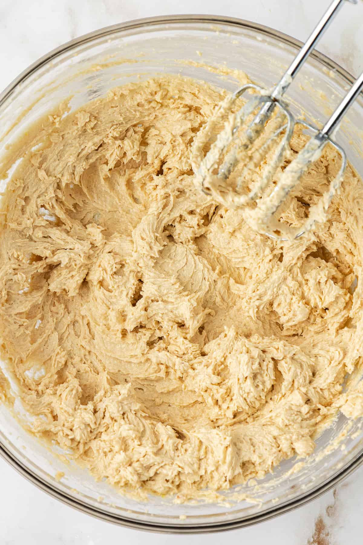 butterscotch cookie dough being mixed with an electric mixer in a clear glass bowl