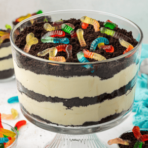 a large trifle dish of dirt cake topped with gummy worms surrounded by smaller dishes of dirt cake, gummy worms and a light teal towel