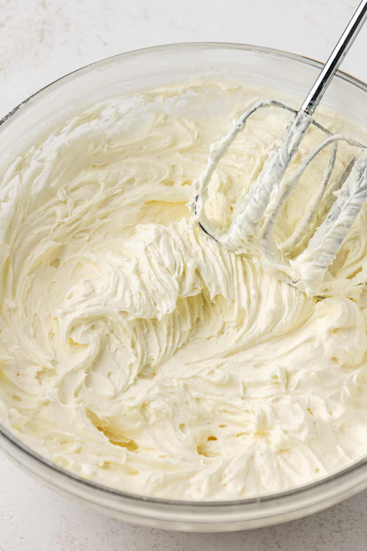 cream cheese, butter and powdered sugar mixed in a clear glass bowl with an electric mixer