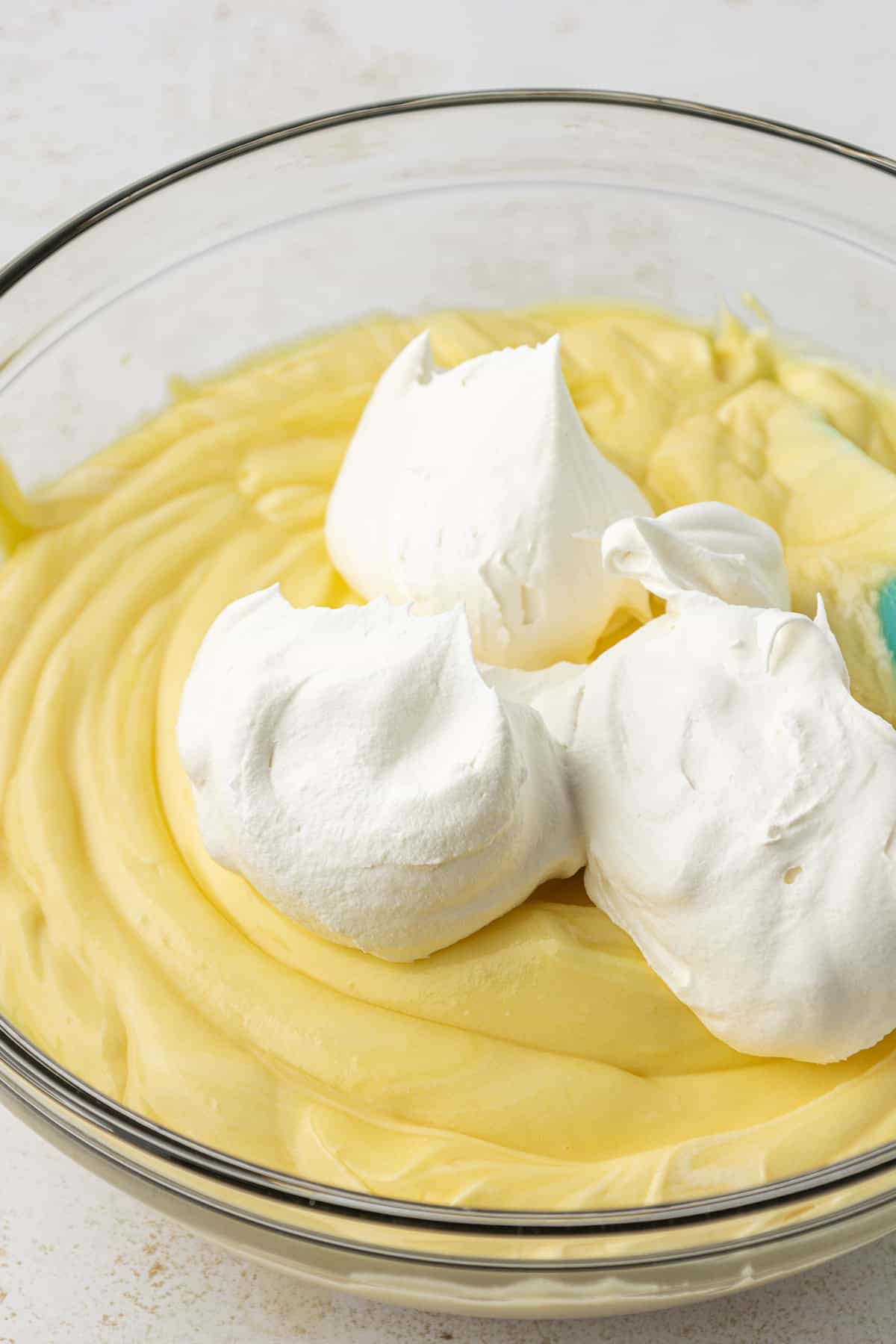 instant vanilla pudding mixture in a clear glass bowl topped with whipped topping that is not mixed in yet