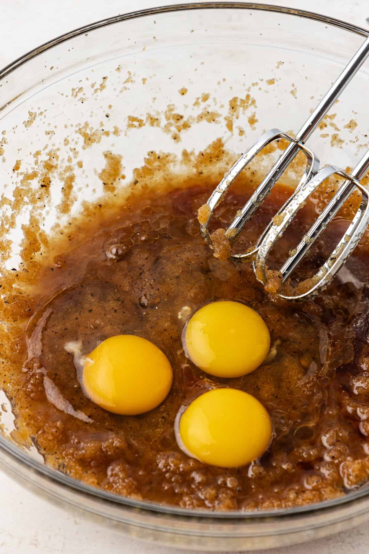 wet ingredients for blondies with three eggs on top in a clear glass bowl with an electric mixer leaning on the side of the bowl