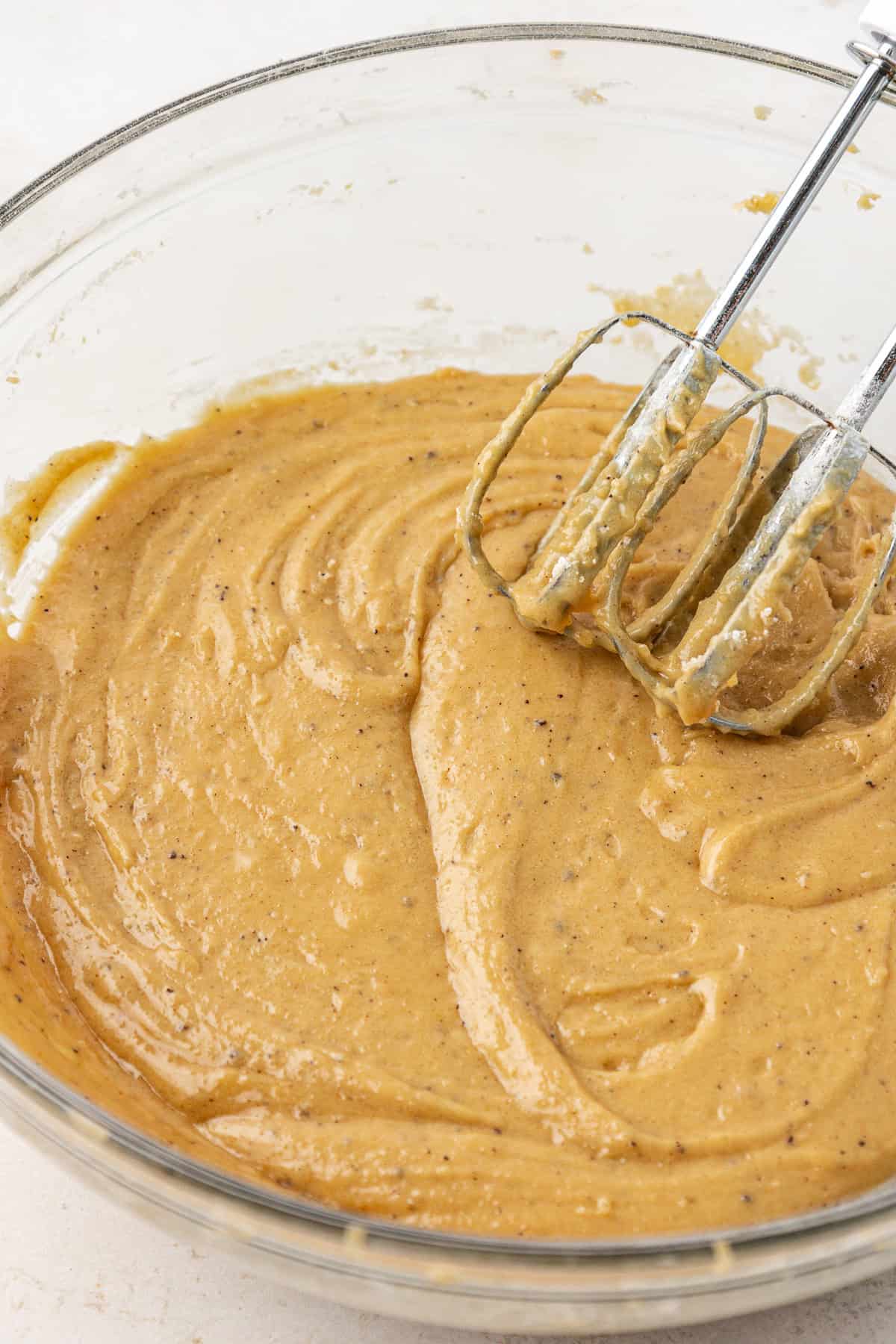 blondie batter mixed in a clear glass bowl with and electric mixer leaning on the side of the bowl