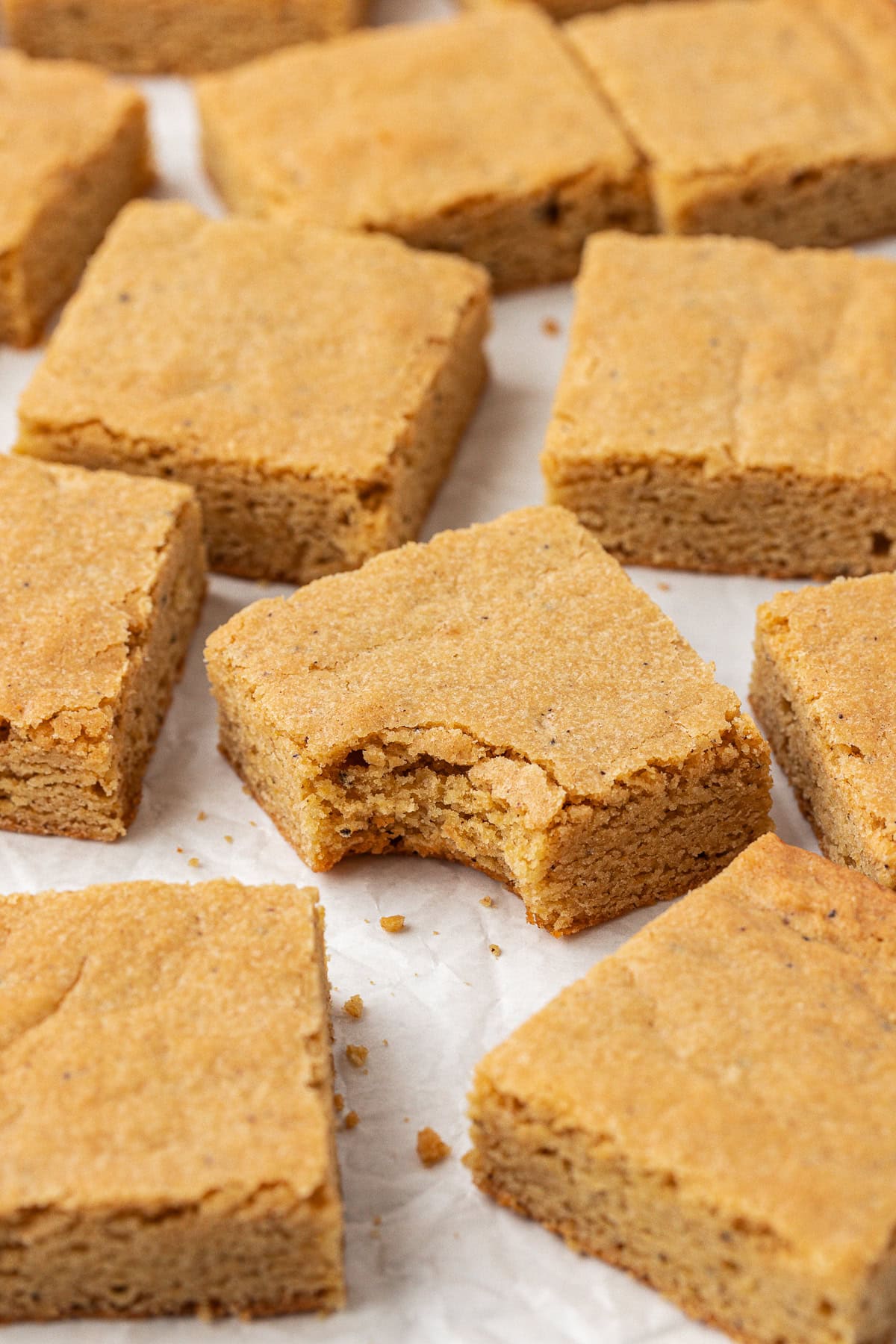 blondies cut in squares and arranged randomly on white parchment paper, with a bite missing out of the middle one