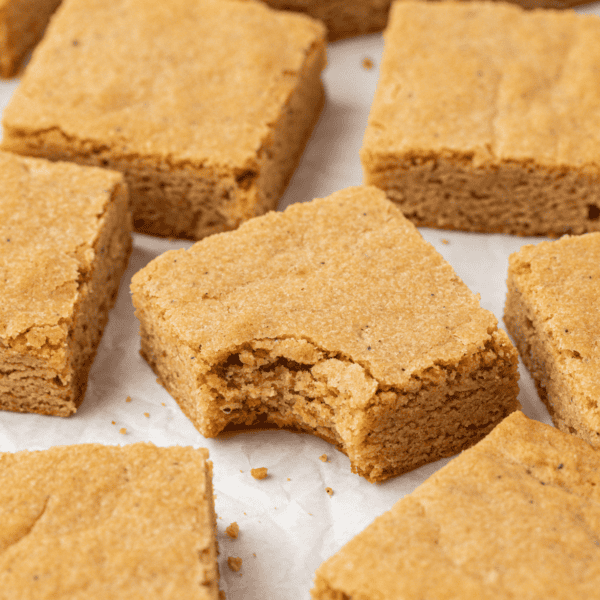 close-up of blondies scattered around each other on white parchment paper with a bite missing out of the center blondie