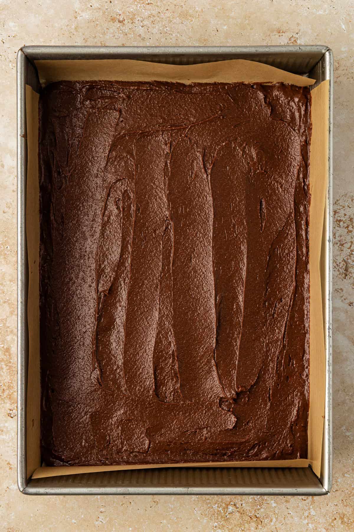 a brown batter layer in a metal pan lined with parchment paper