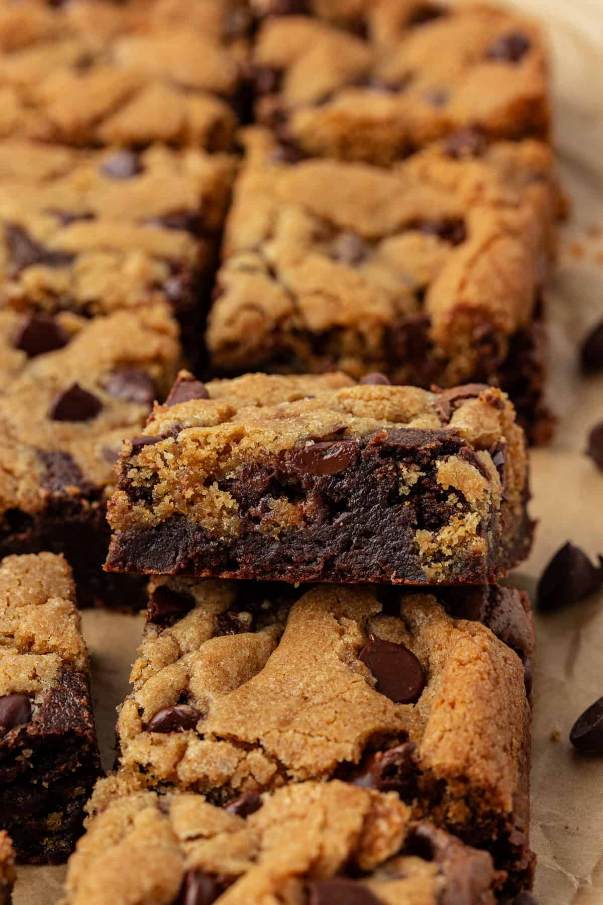 rows of brookies on brown parchment paper, with one leaning on top of another showing the two layers with brownie on the bottom and chocolate chip cookie on top