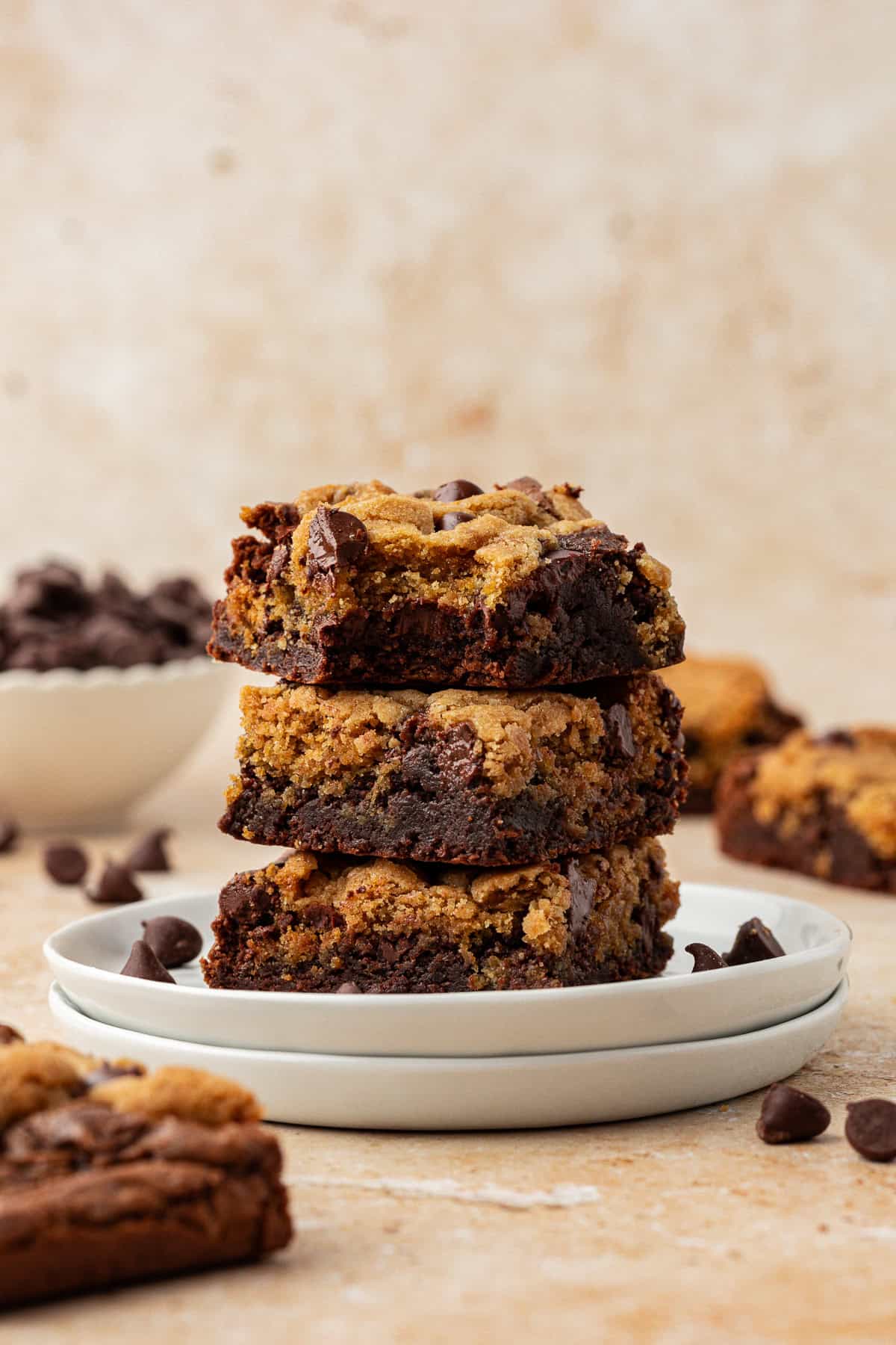 three brookies stacked in a tower on top of two small white plates stacked with more brookies and chocolate chips scattered around