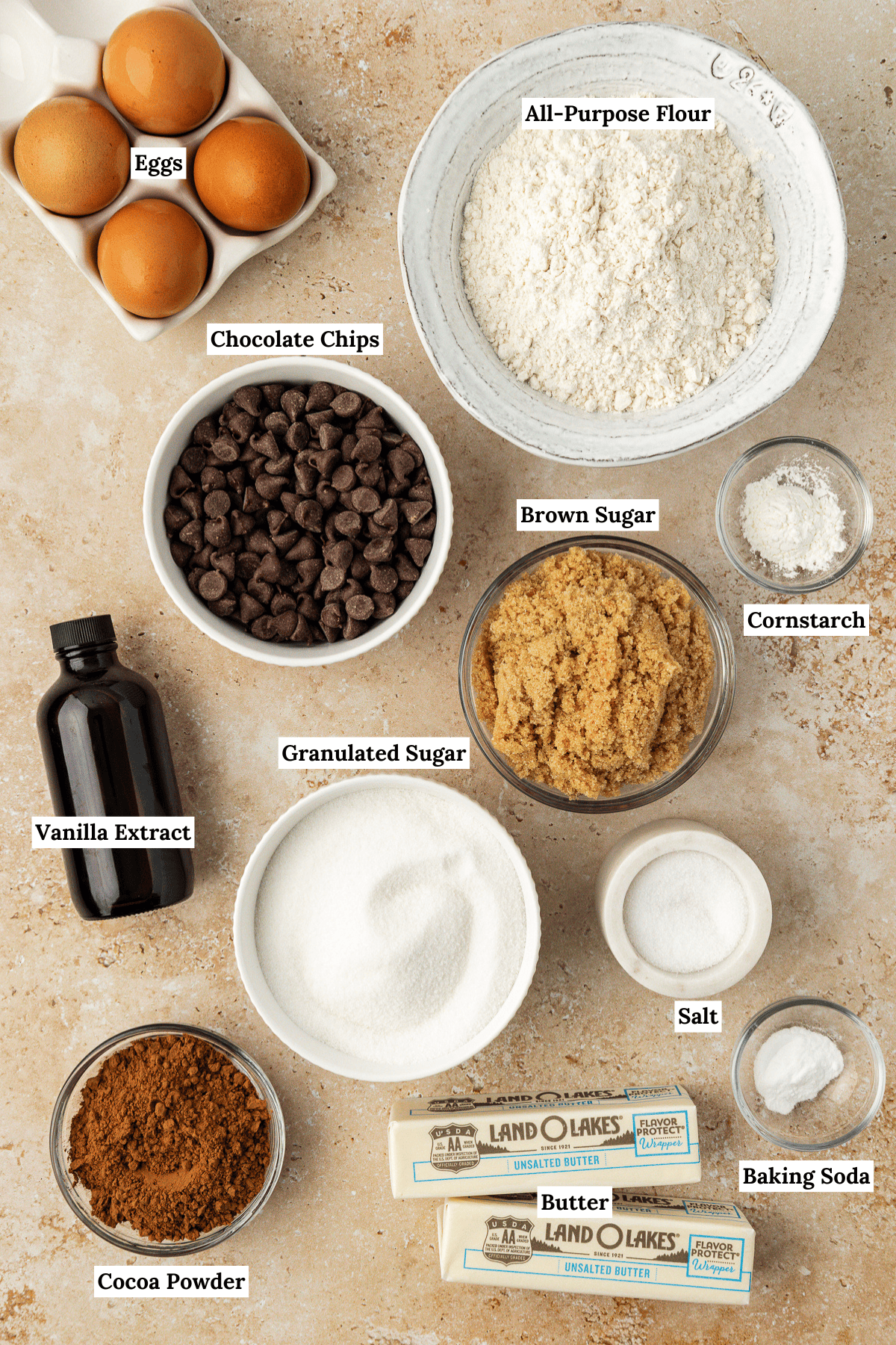 overhead view of the ingredients for brookies including eggs, all-purpose flour, chocolate chips, vanilla extract, brown sugar, cornstarch, granulated sugar, cocoa powder, butter, salt and baking soda