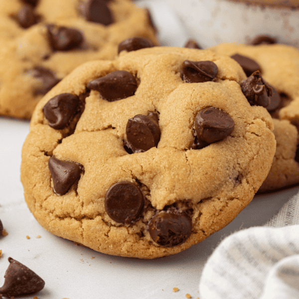 close up of a peanut butter chocolate chip cookie leaning on another cookie with more in the background, and chocolate chips and cookie crumbs scattered around