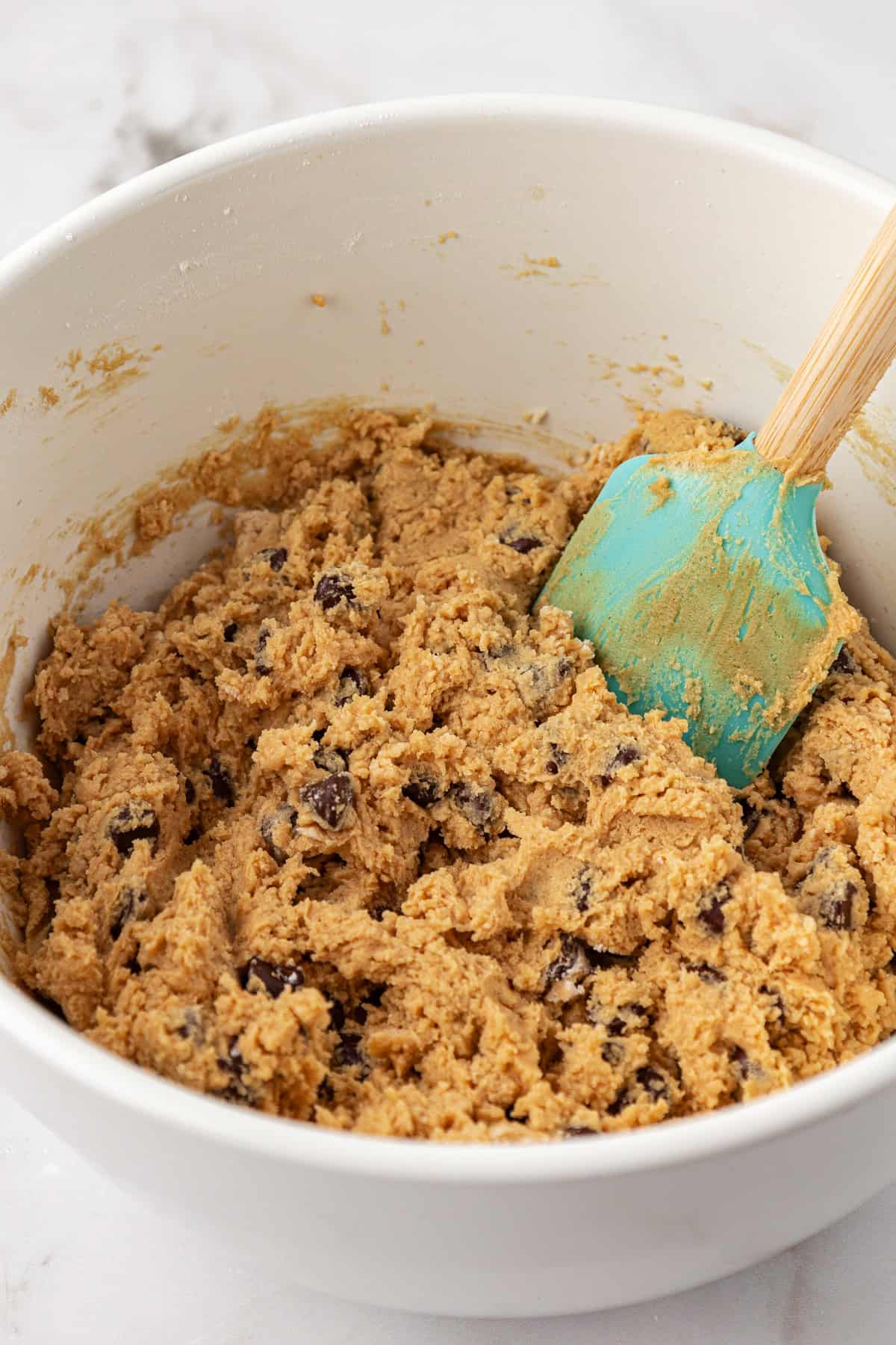 peanut butter chocolate chip cookie dough in a large white bowl with a teal spatula