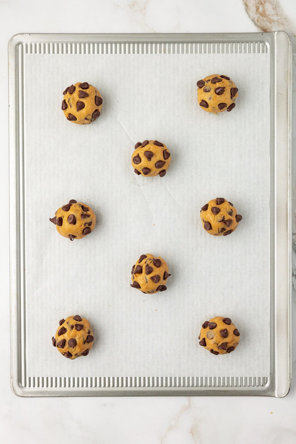 overhead view of a baking sheet lined with white parchment paper with peanut butter chocolate chip cookie dough balls spaced in rows on top