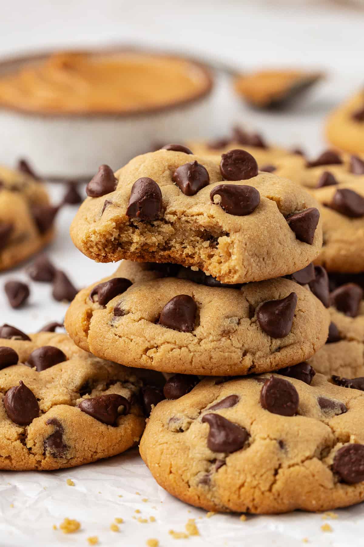 a stack of peanut butter chocolate chip cookies on white parchment paper, with a bite missing out of the top cookie