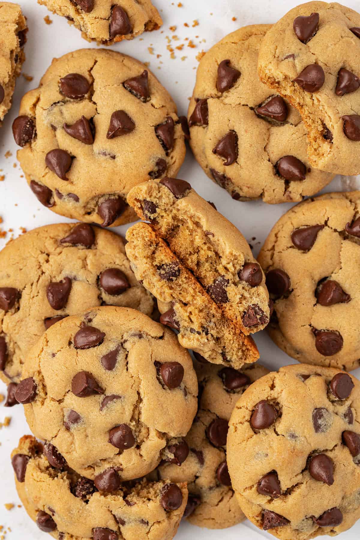 over head view of piles of peanut butter chocolate chip cookies, with one cookie in the middle split in half, standing up showing its inside