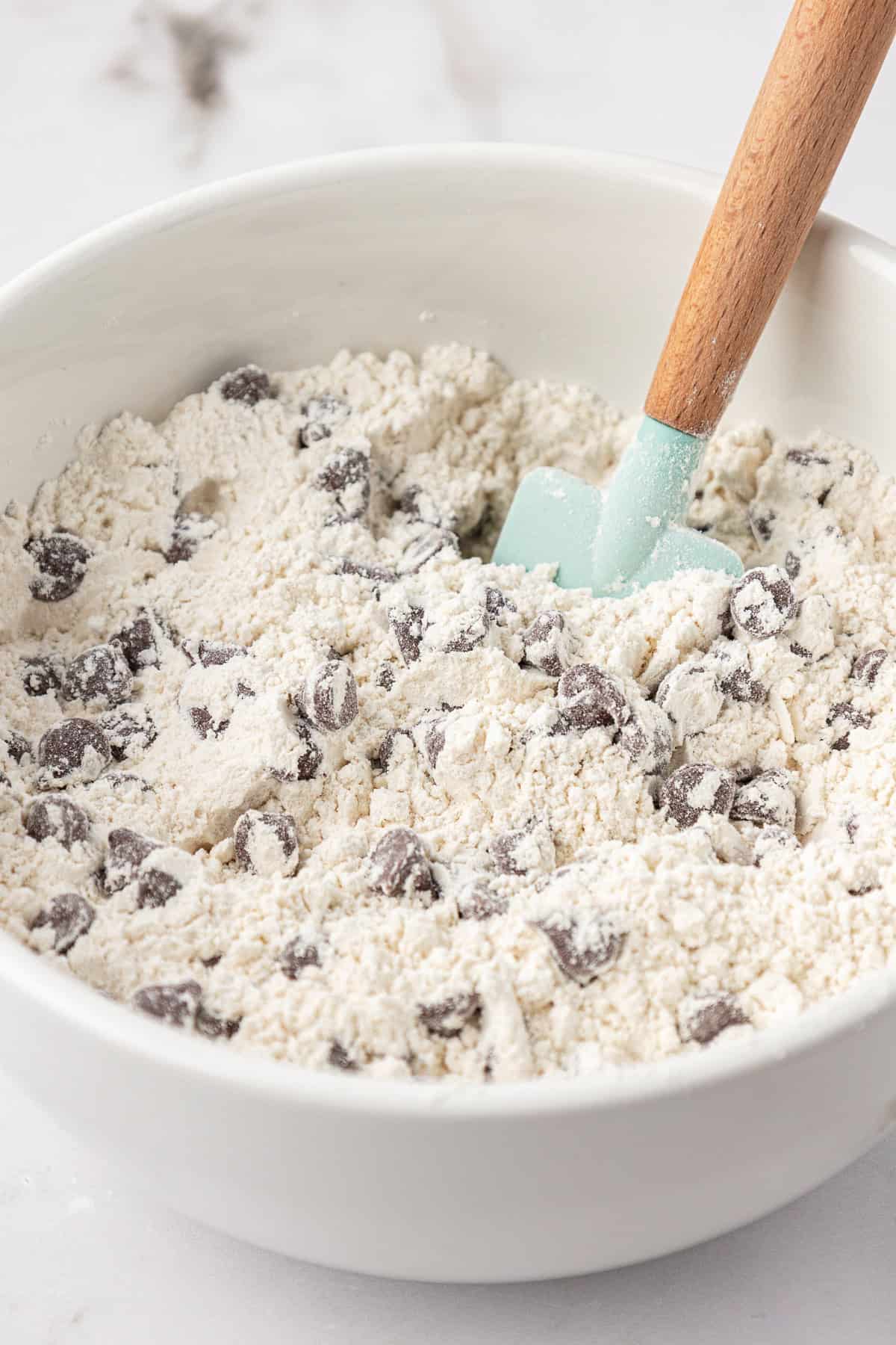 flour mixture and chocolate chips mixed in a white bowl with a teal spatula