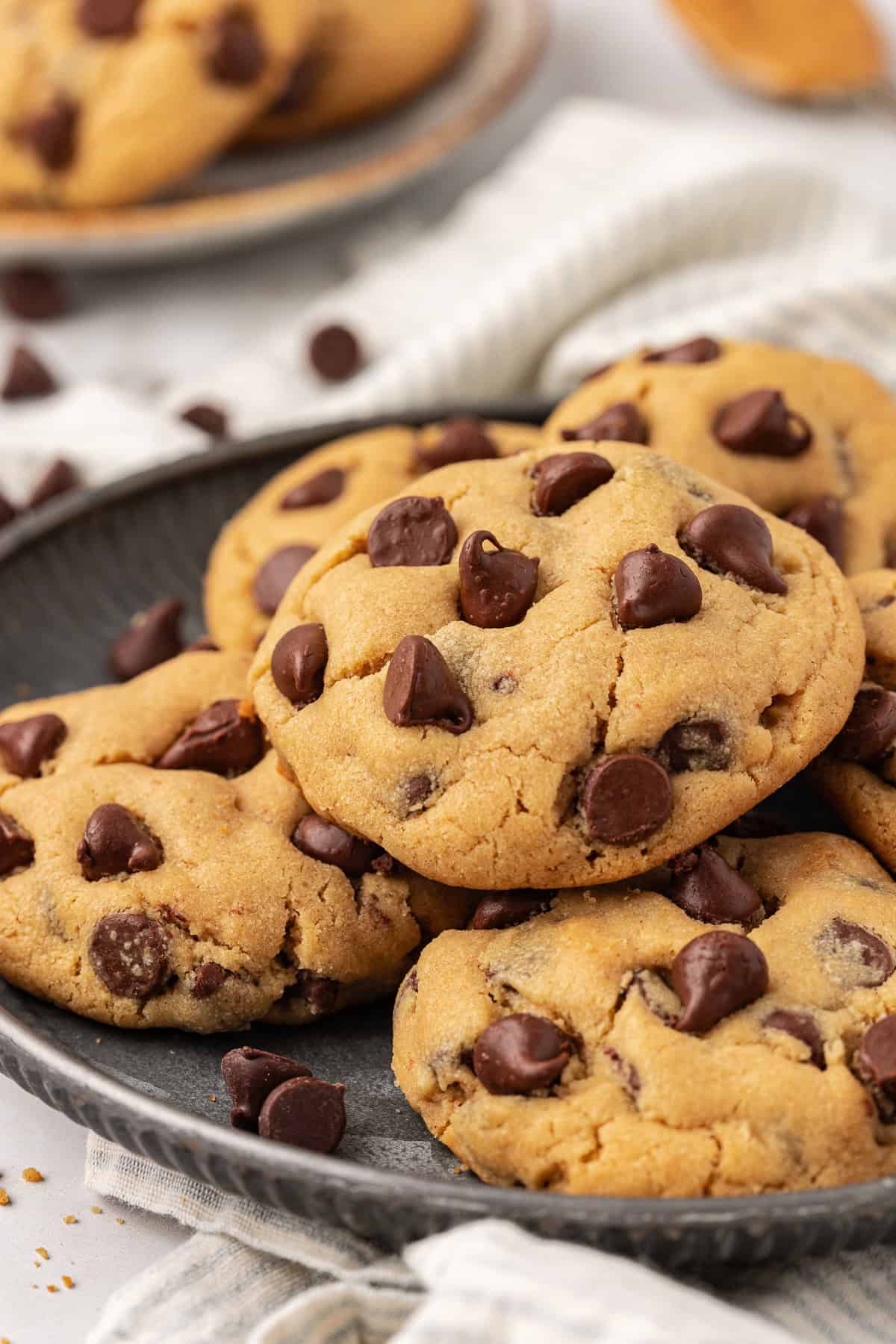 a plate full of peanut butter chocolate chip cookies on top of a white and grey striped kitchen towel with chocolate chips sprinkled around