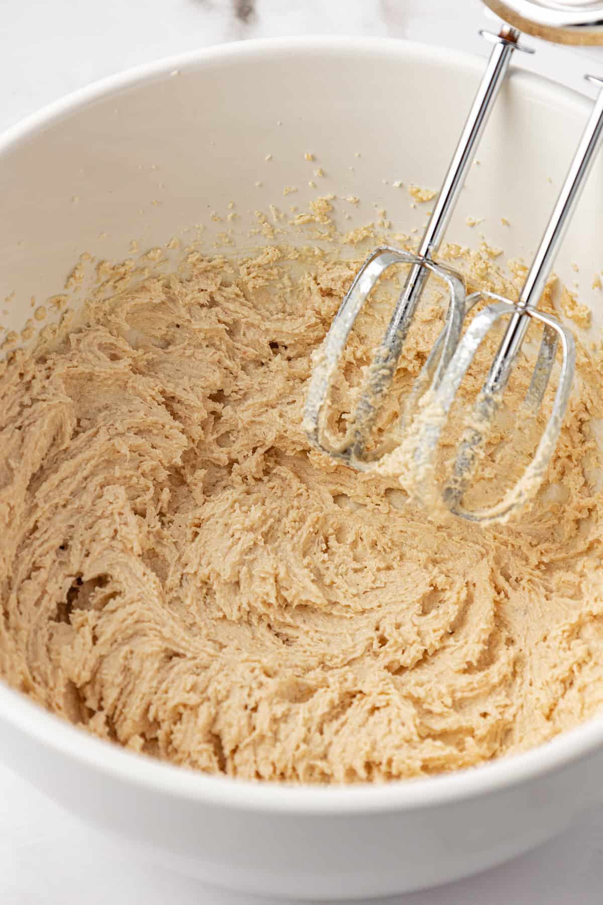 cookie dough being mixed in a white bowl with an electric mixer