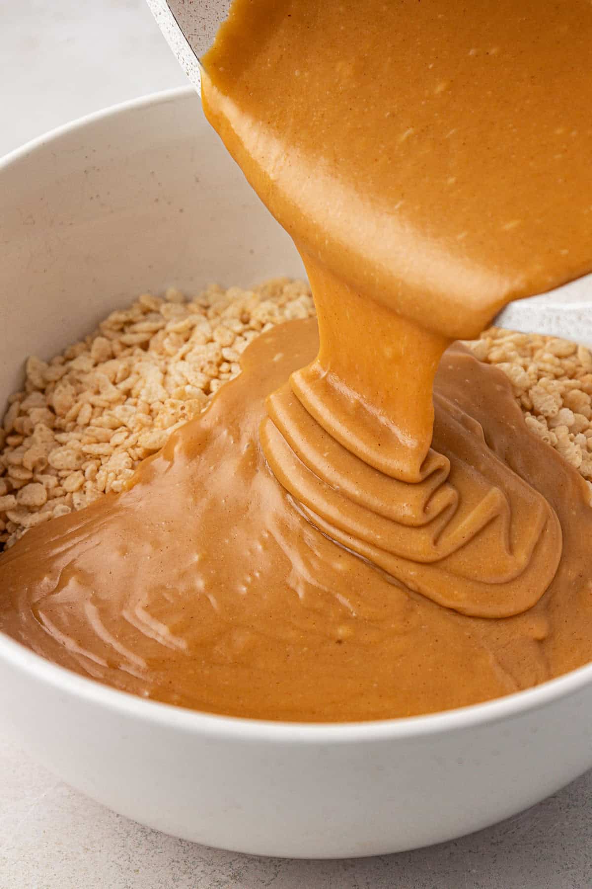 a creamy peanut butter mixture being poured over top of rice cereal in a white bowl