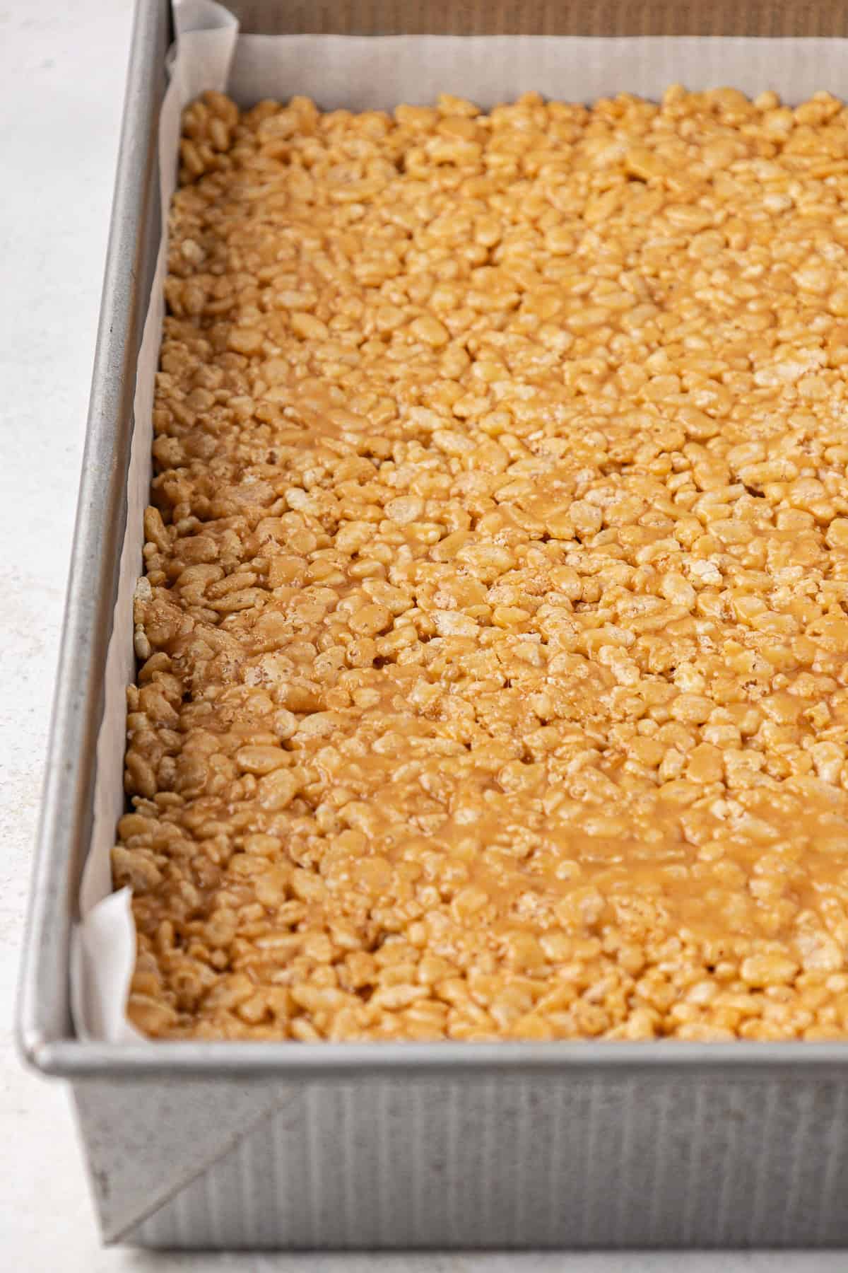 a baking dish lined with parchment paper and packed with a rice krispie mixture