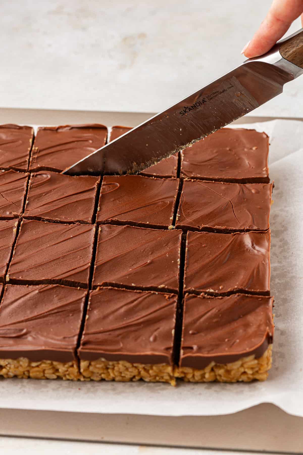 Scotcheroo bars being sliced into squares on white parchment paper