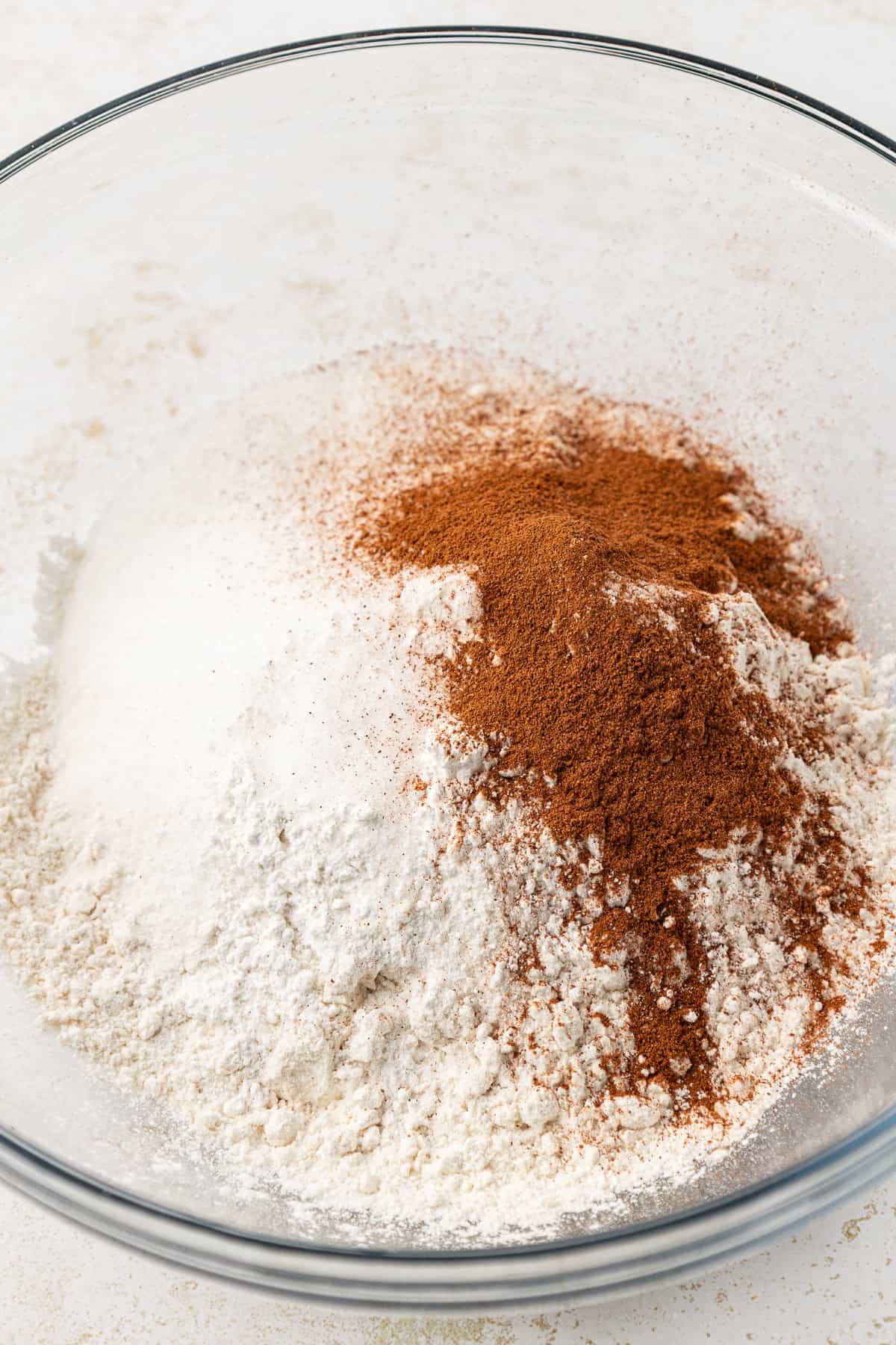 dry ingredients for apple fritters, not yet mixed together, in a clear glass bowl