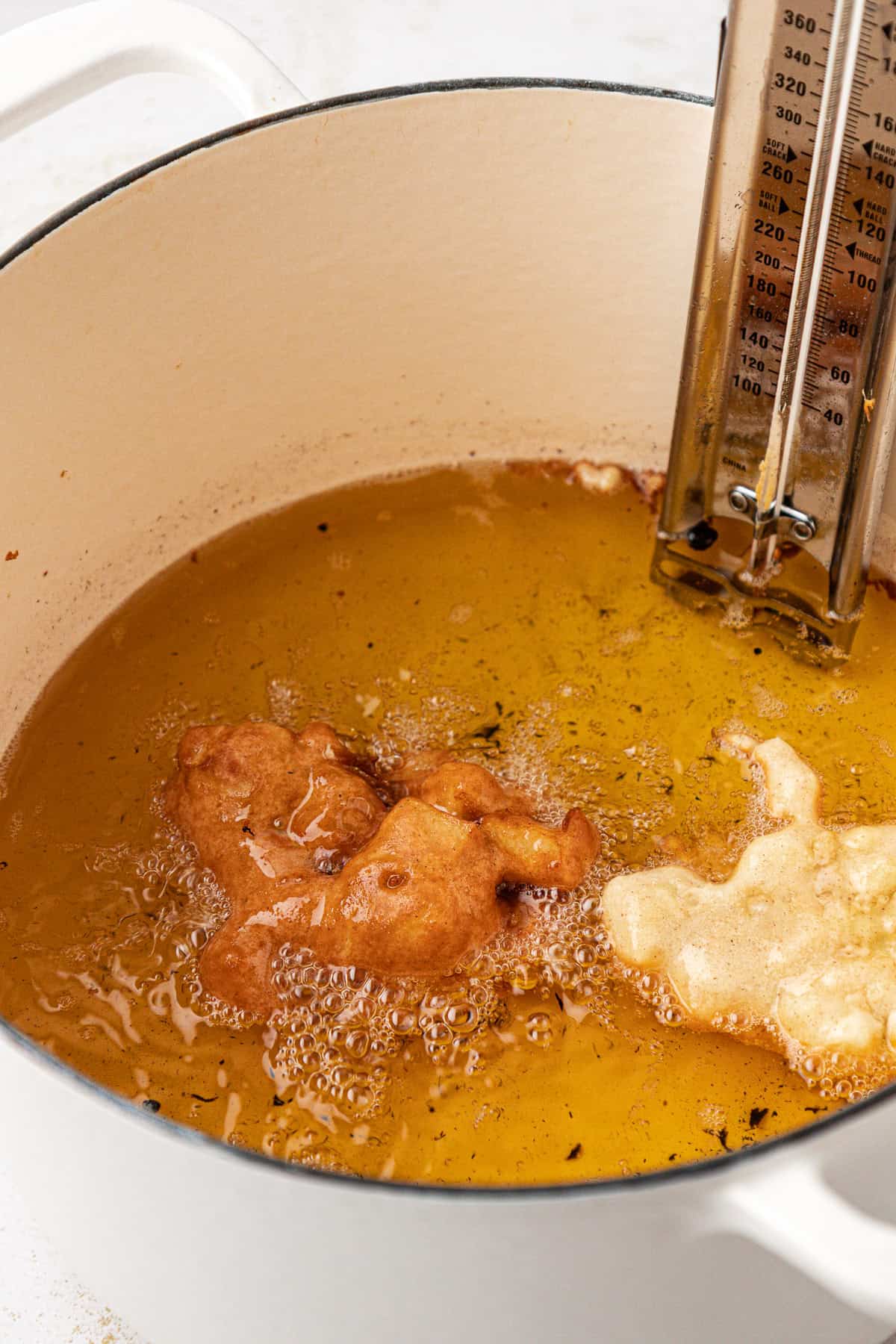 apple fritters frying in a pot of hot oil with a thermometer in it