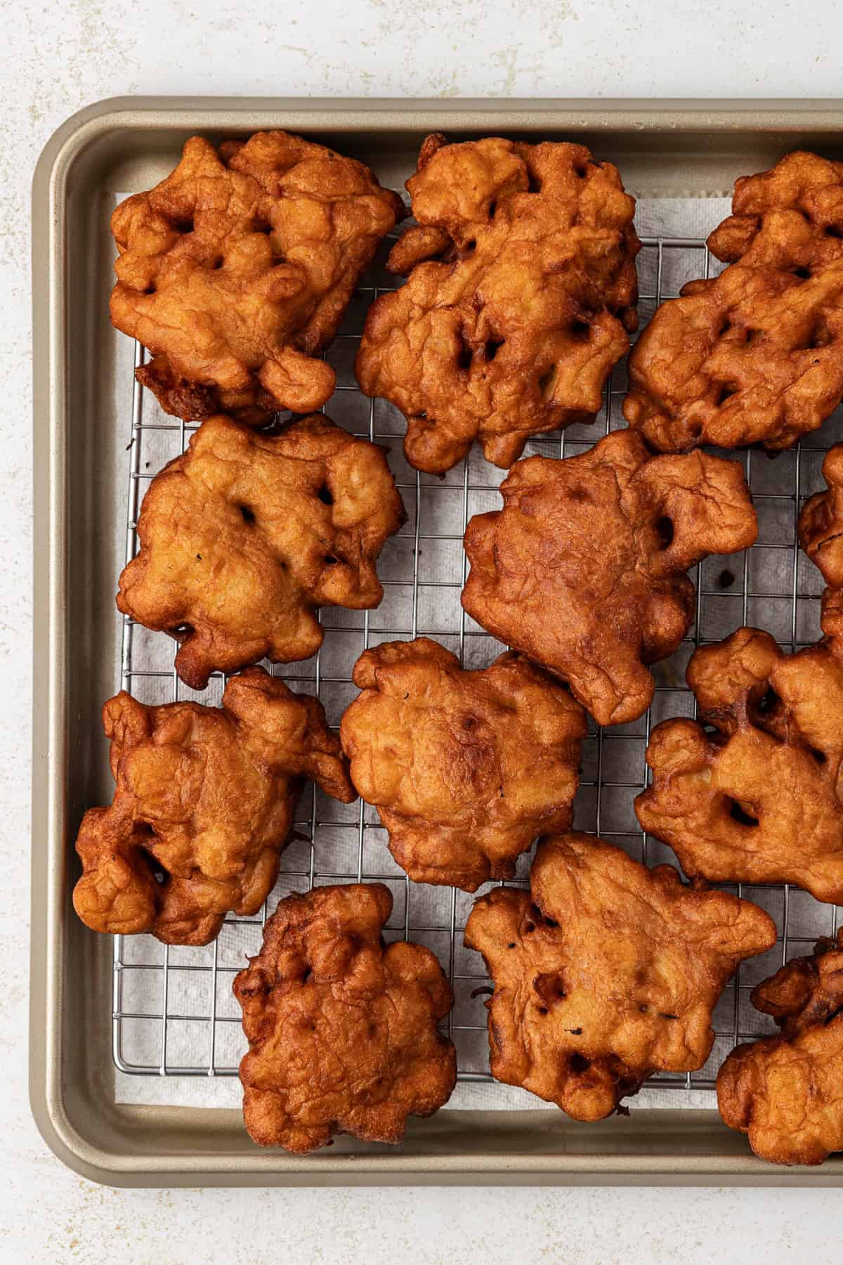 apple fritters on a wire rack on top of a baking sheet lined with paper towels