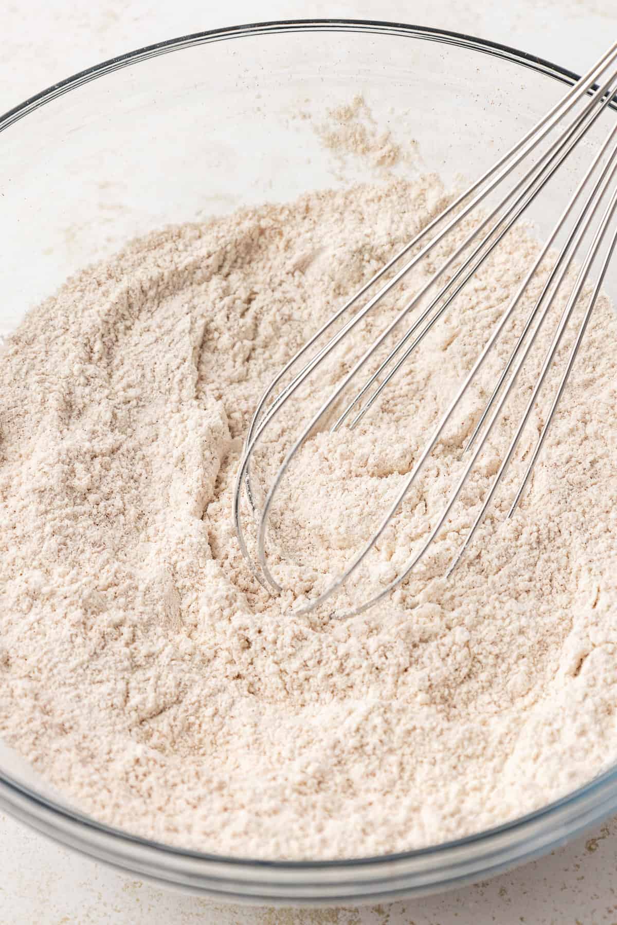 dry ingredients for apple fritters in a clear glass bowl with a whisk