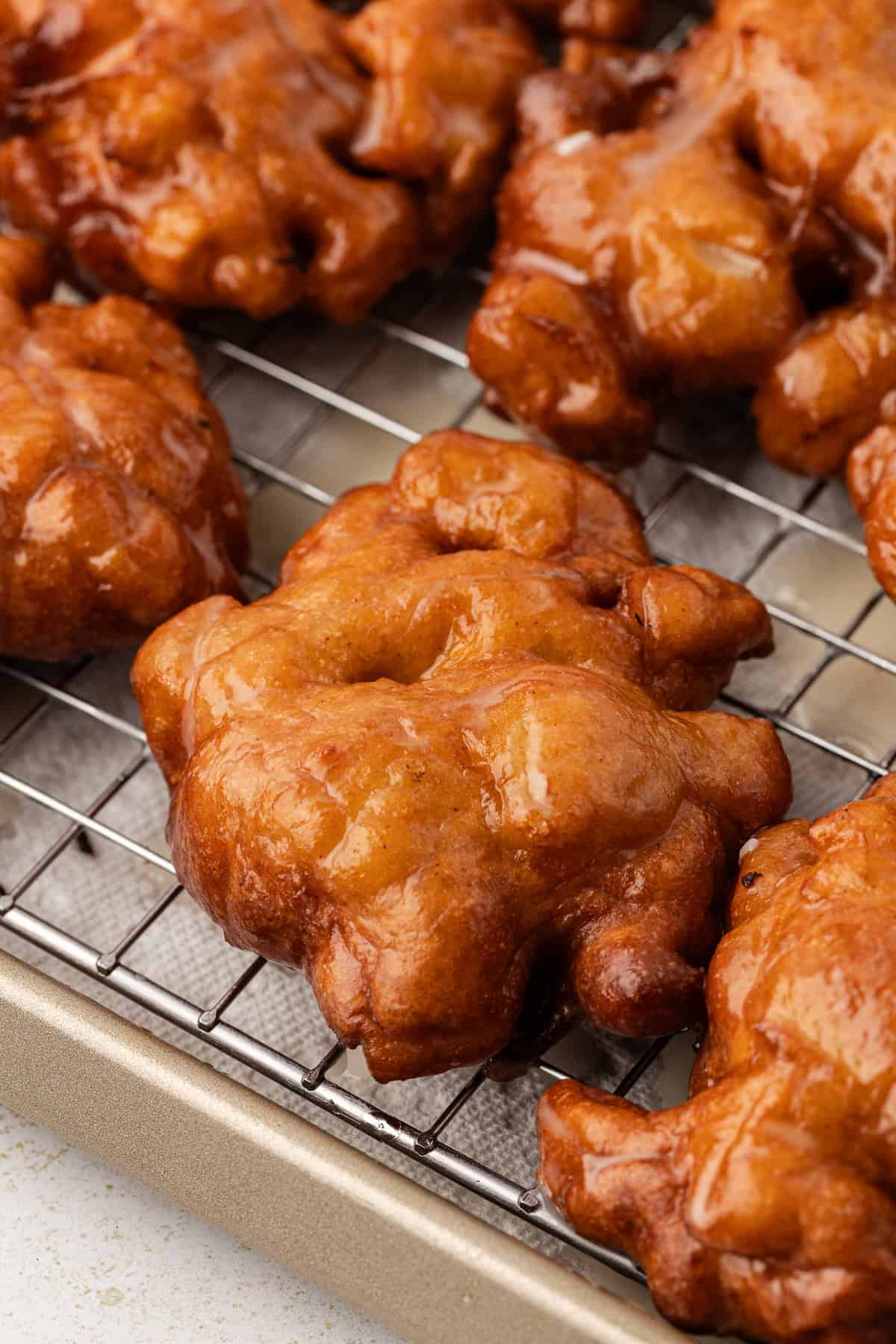 close up of apple fritters on a wire rack on top of a baking sheet lined with paper towels