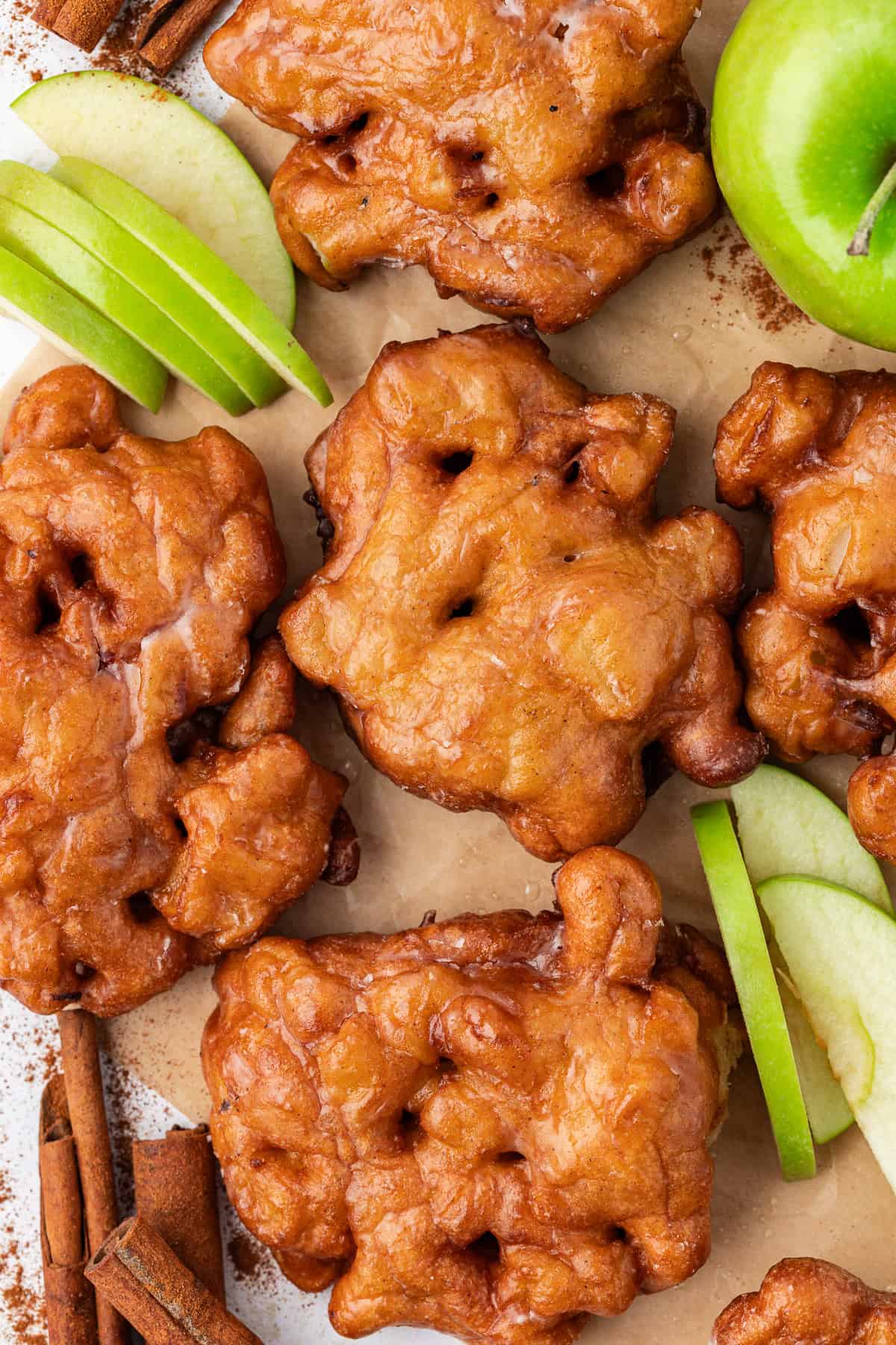 apple fritters scattered over brown paper with fresh green apple slices, cinnamon sticks and a whole green apple