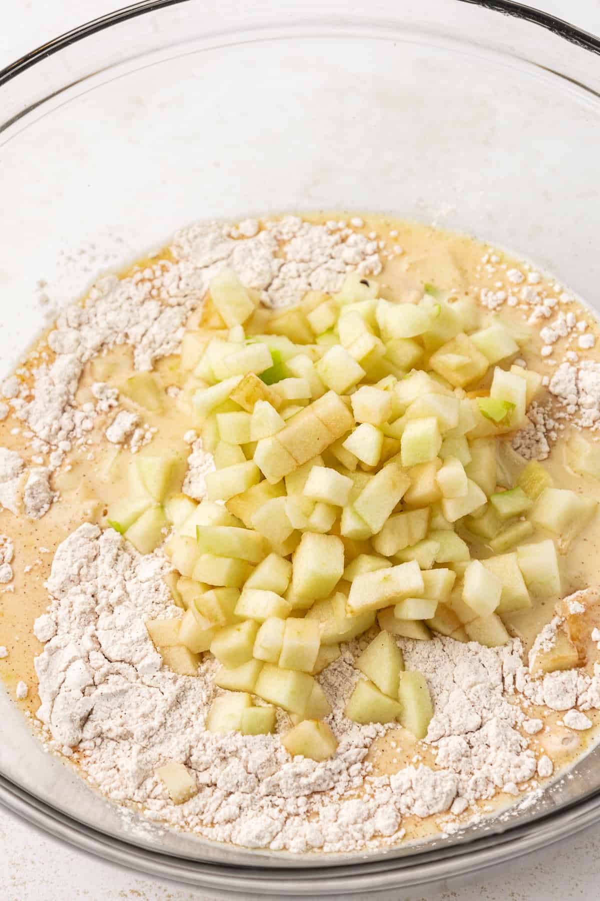 chopped apples and the dry and wet ingredients for apple fritter, not yet combined, in a large clear glass bowl