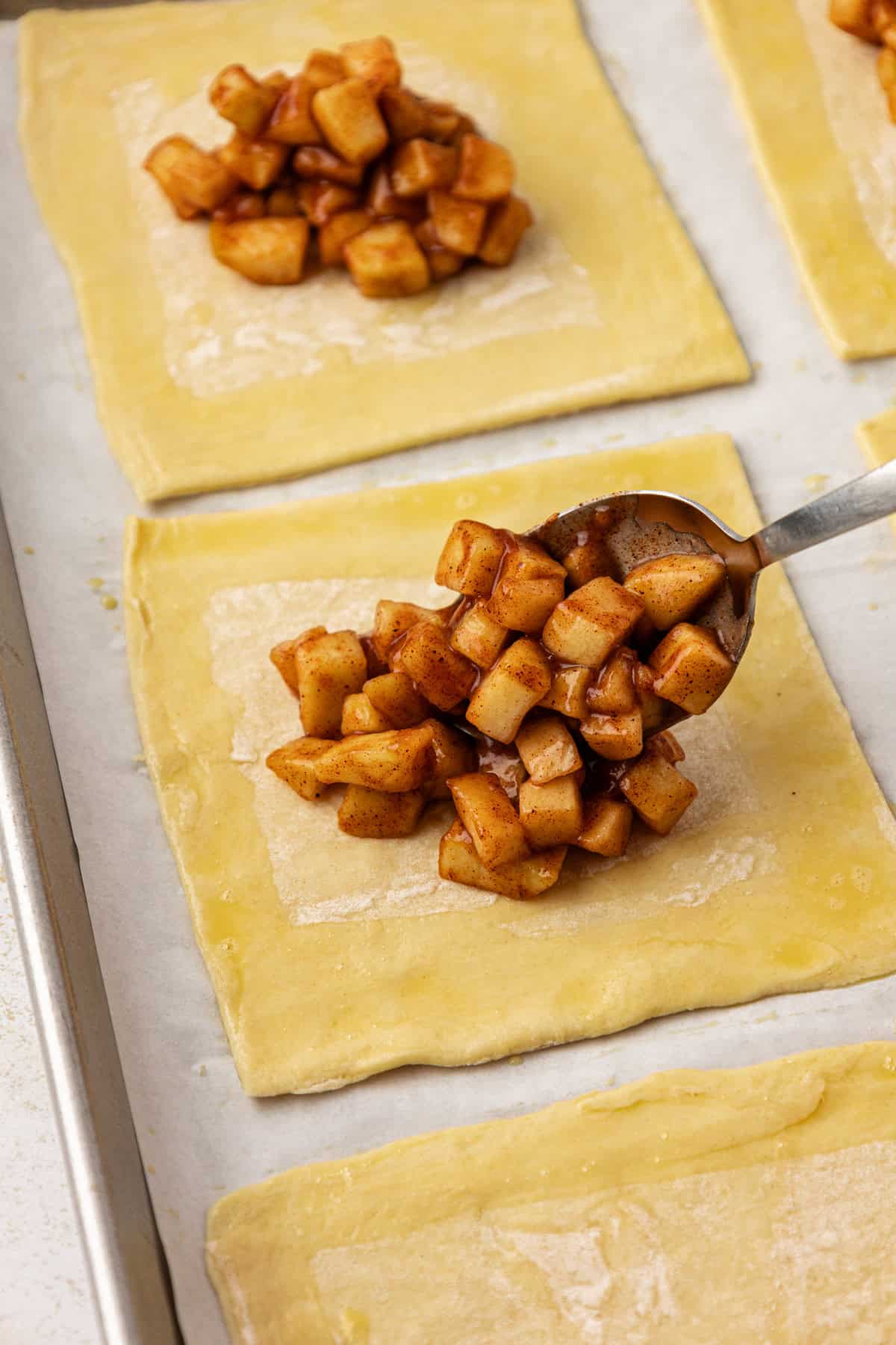 apple filling mixture being spooned onto a square of puff pastry on a baking sheet lined with parchment paper