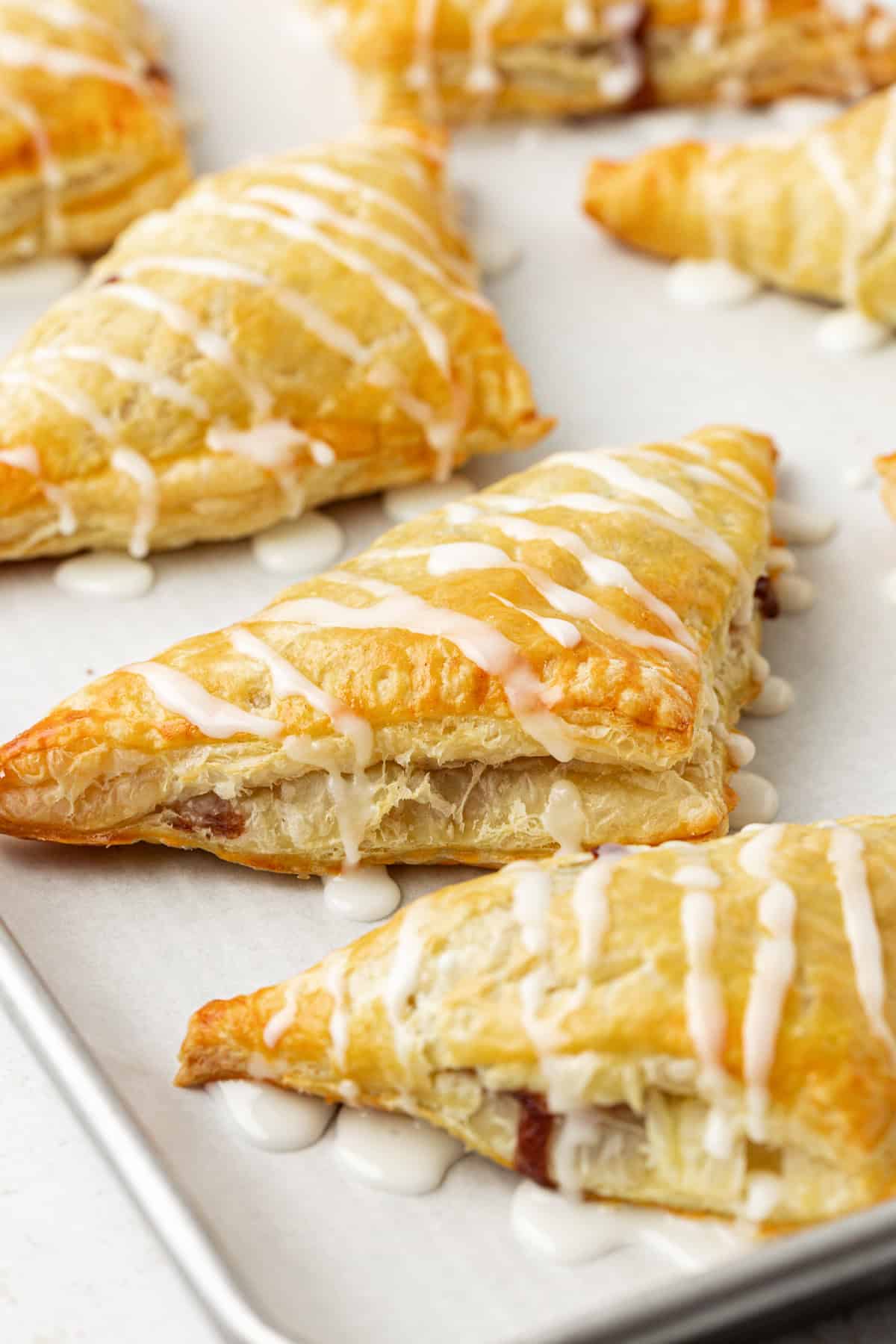 close up of apple turnovers drizzled with glaze on a baking sheet lined with parchment paper