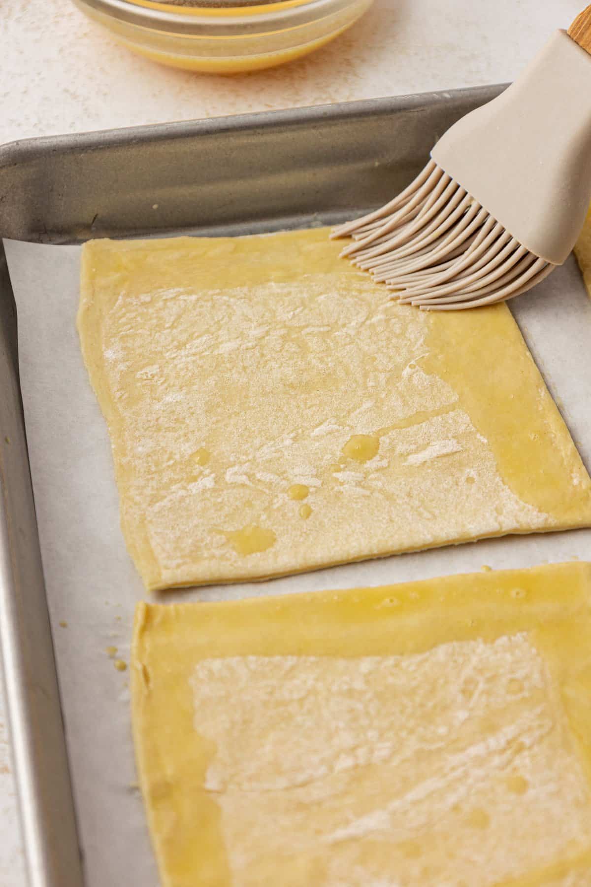 brushing the edges of puff pastry squares with egg wash