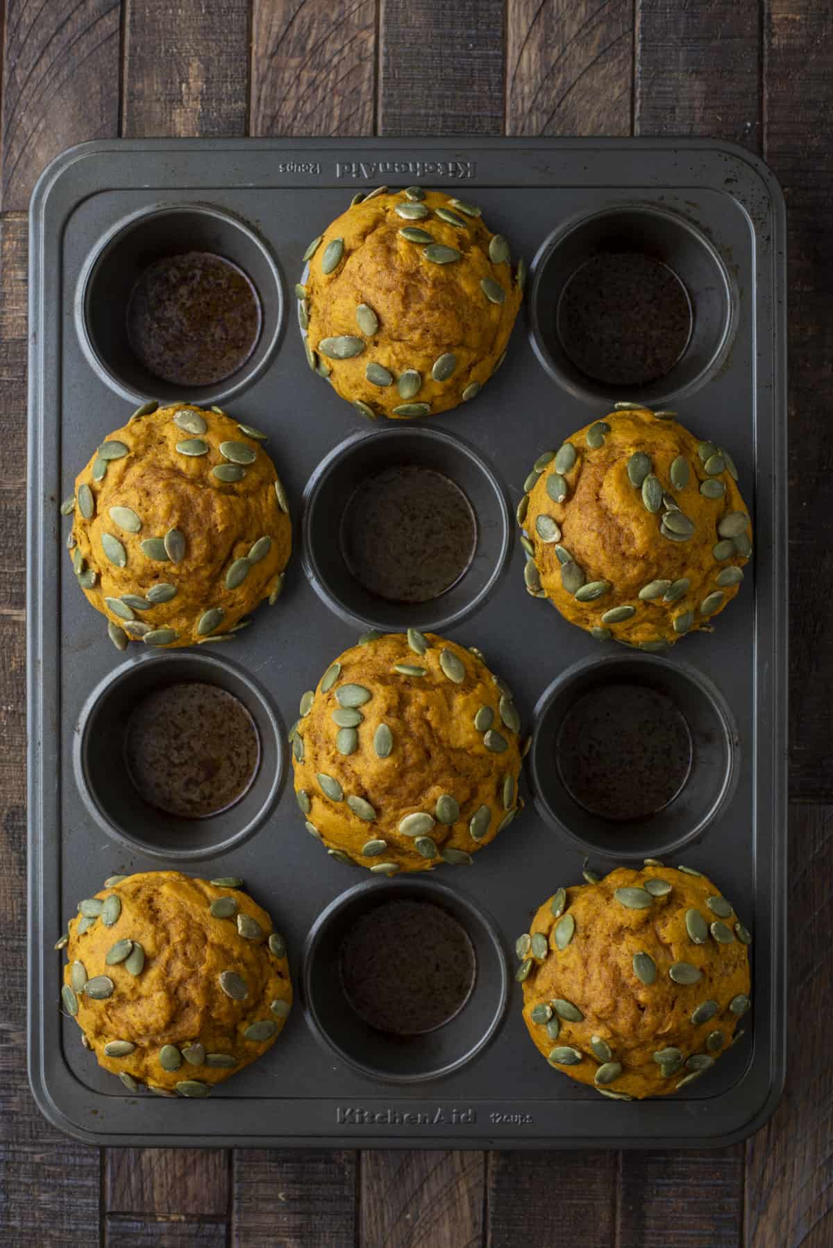 freshly baked pumpkin muffins topped with pumpkin seeds in every other hole of a muffin pan